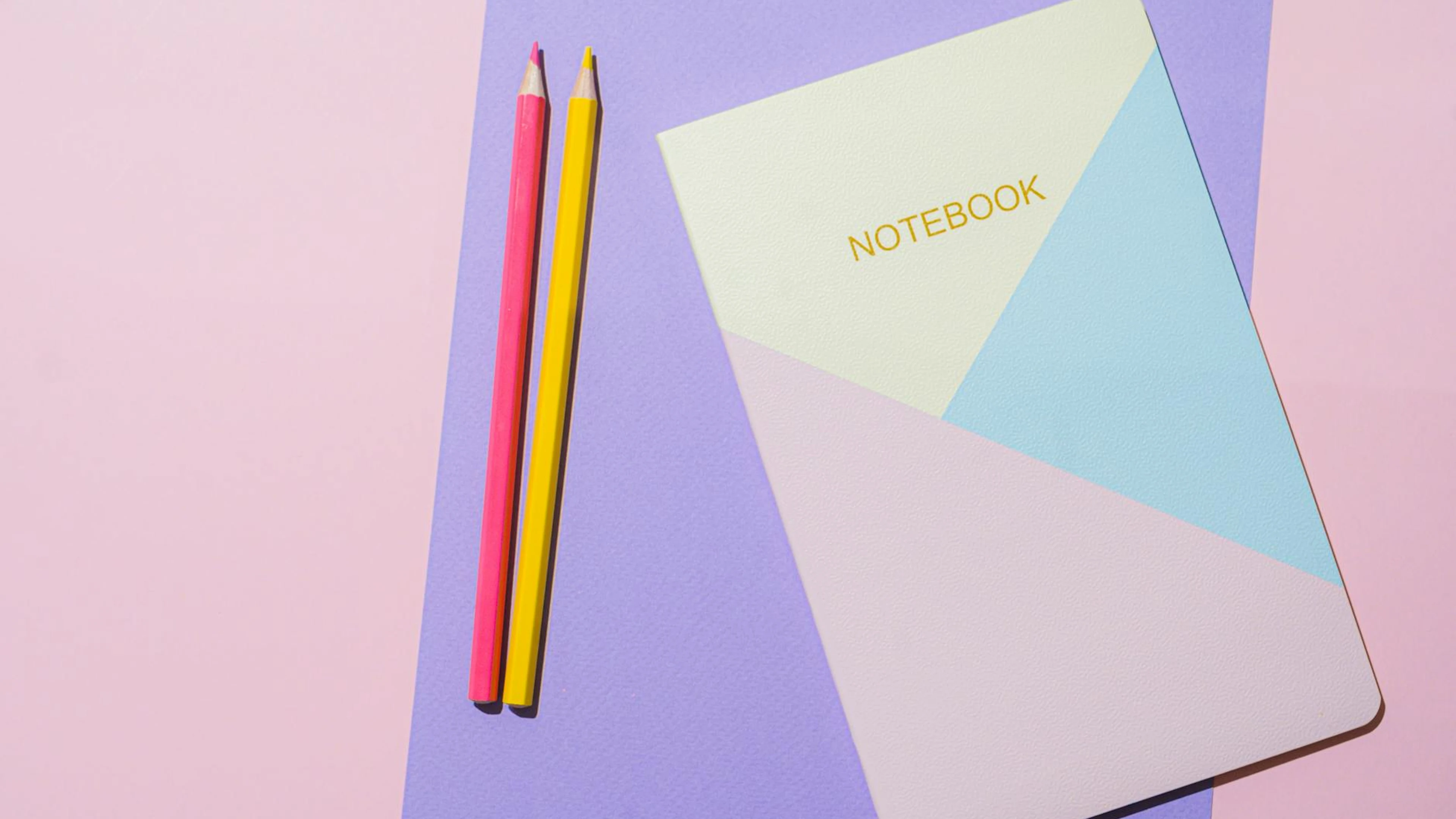A minimalist flat lay of a geometric notebook and colored pencils on pastel back - free 4K Ultra HD aesthetic wallpaper for desktop