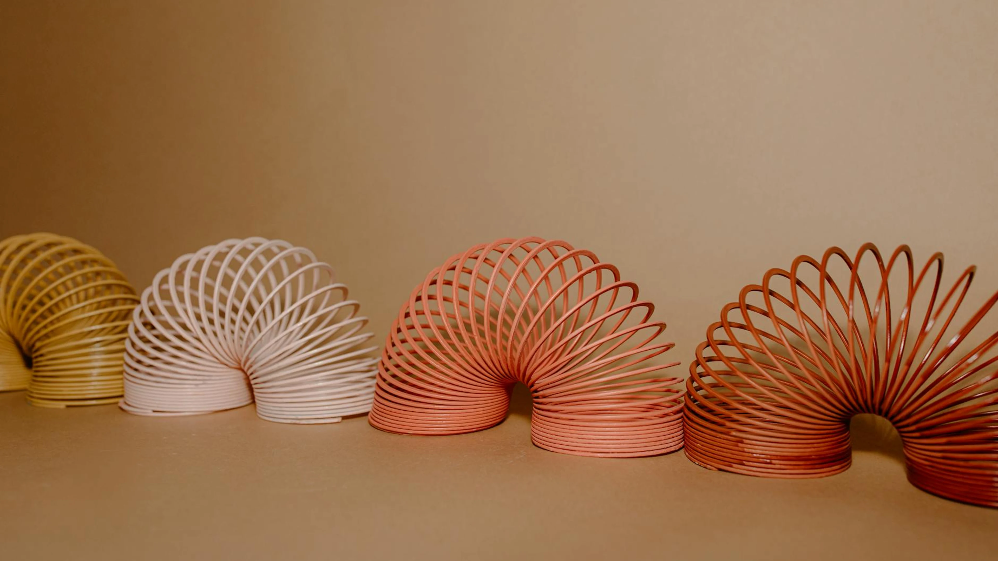 A vibrant row of Slinkies displaying gradient rainbow colors on a neutral backdr - free 4K Ultra HD aesthetic wallpaper for desktop