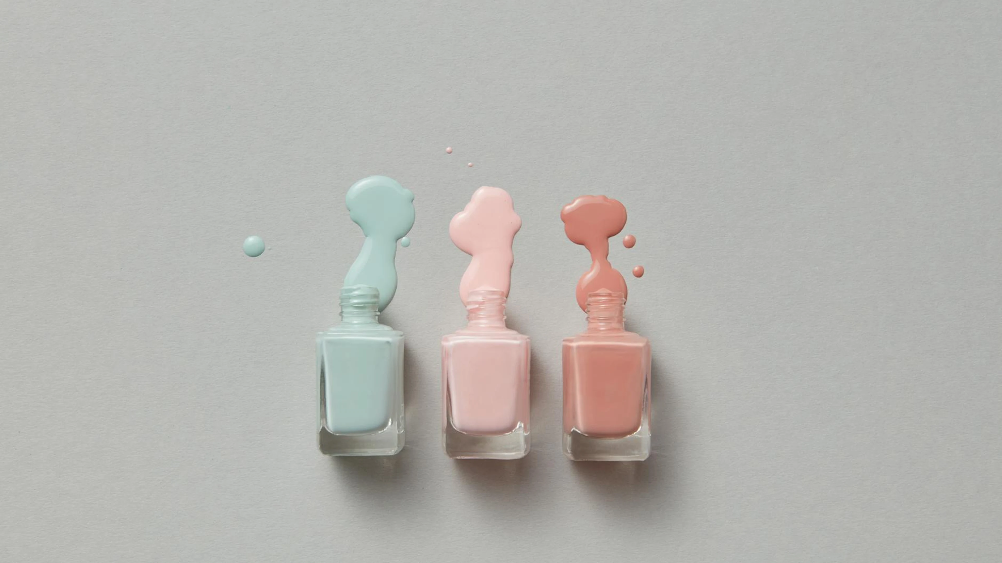 Pastel nail polish bottles with vibrant spills on a gray background. - free 4K Ultra HD aesthetic wallpaper for desktop