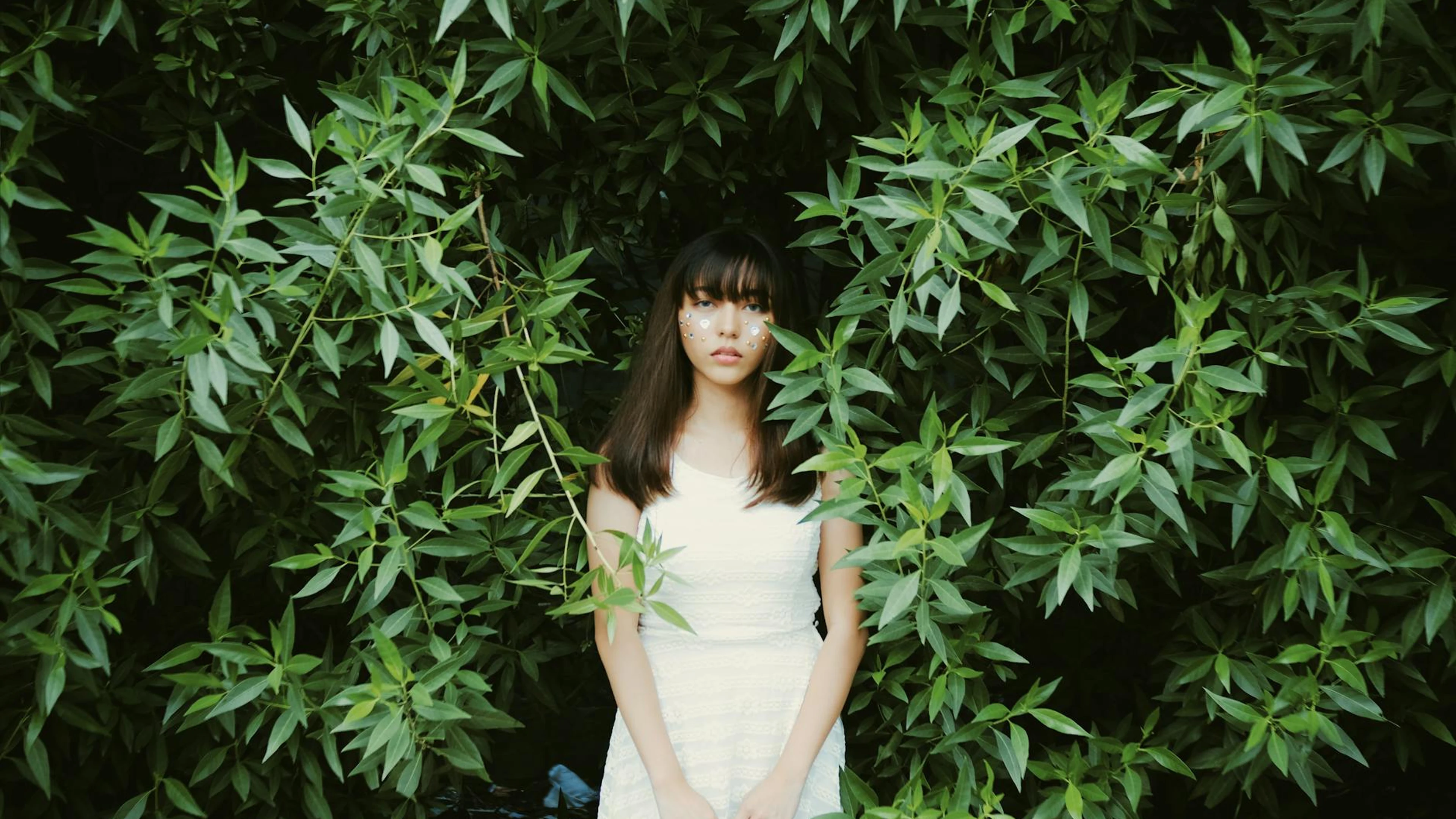 Young woman in white dress standing amidst vibrant green leaves, evoking a sense - free 4K Ultra HD aesthetic wallpaper for desktop