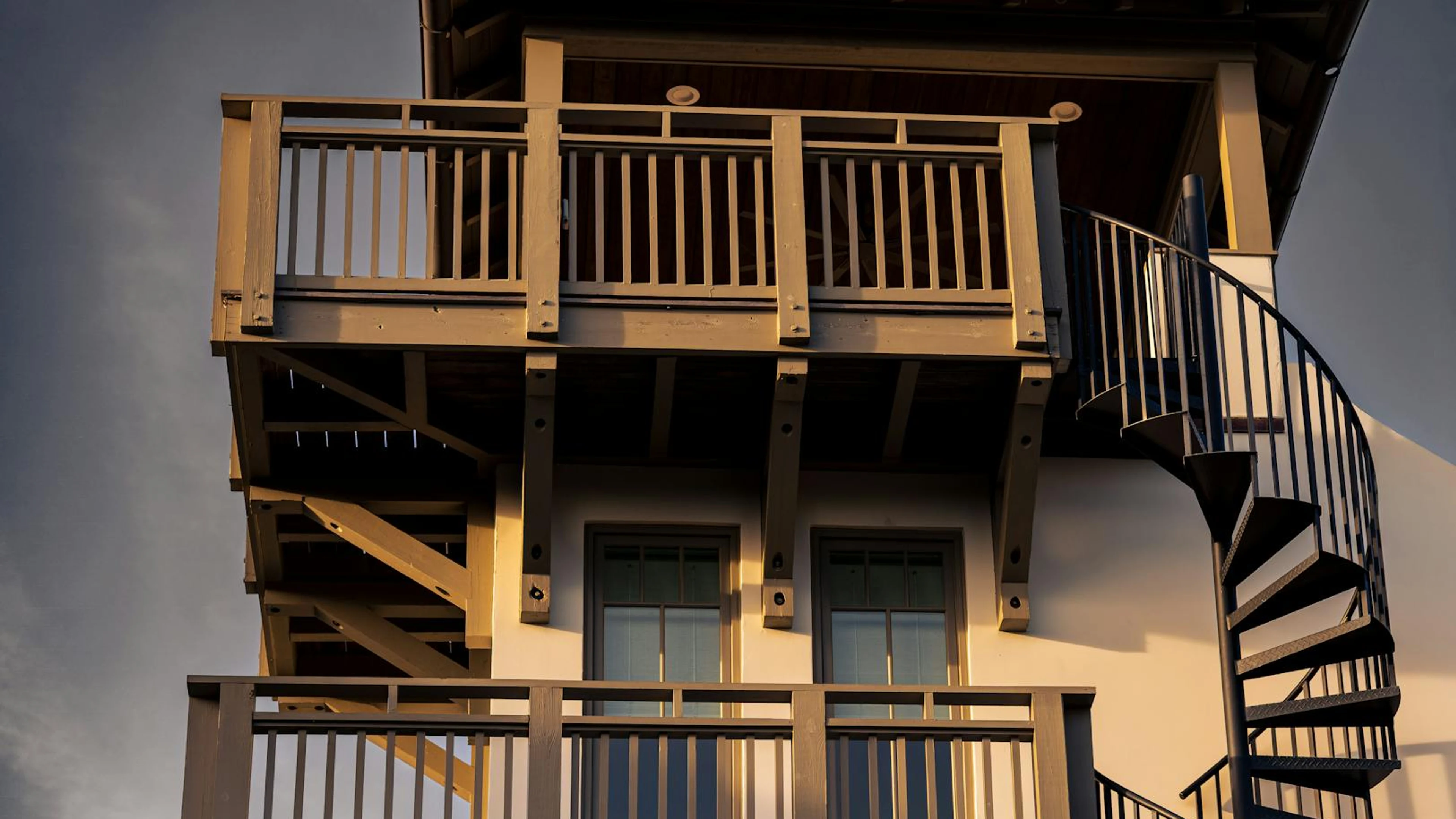 A rustic wooden balcony with a spiral staircase illuminated by warm sunset light - free 4K Ultra HD architecture wallpaper for desktop