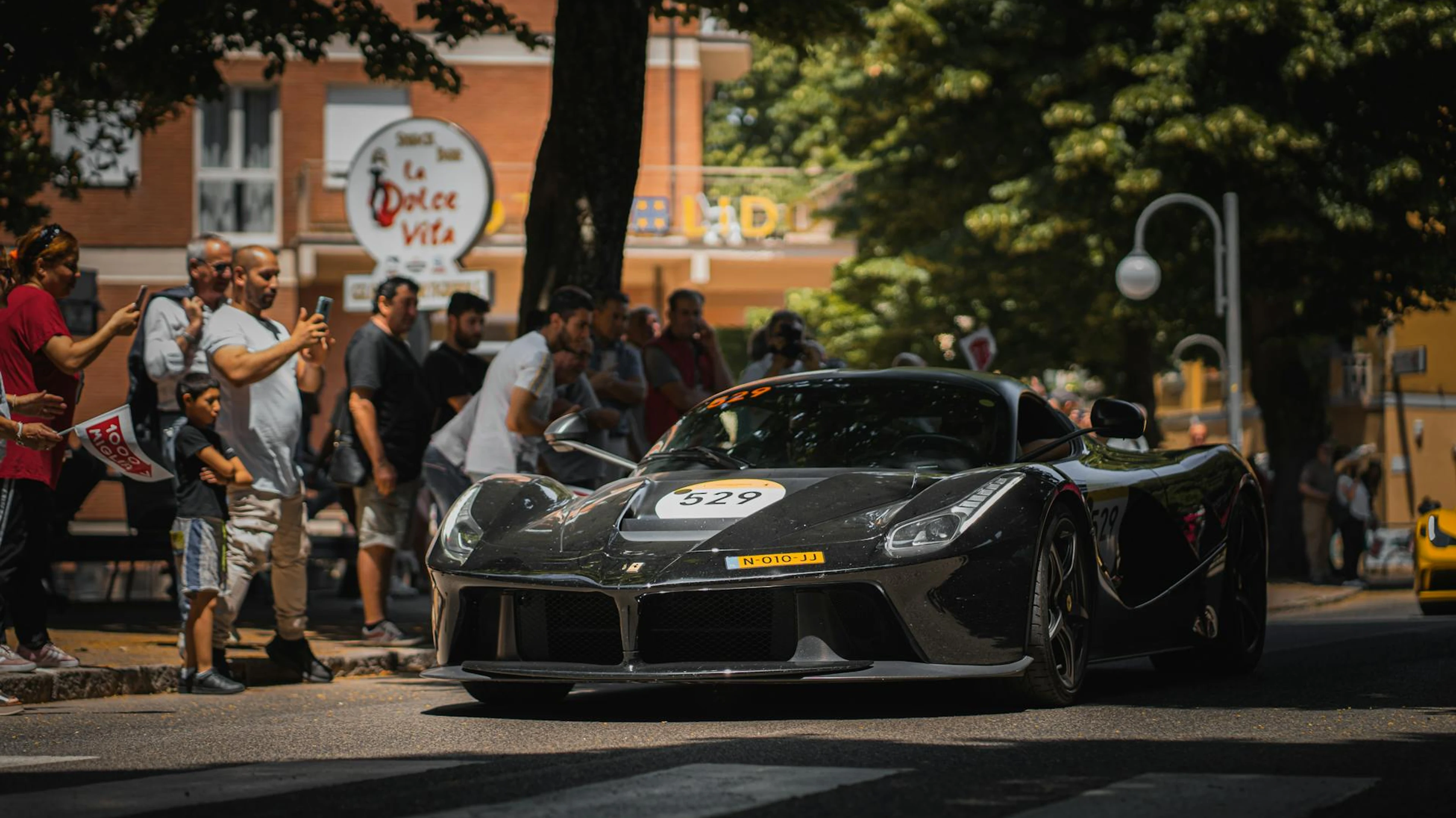 A black sports car driving through city streets during a public automotive event - free 4K Ultra HD cars wallpaper for desktop