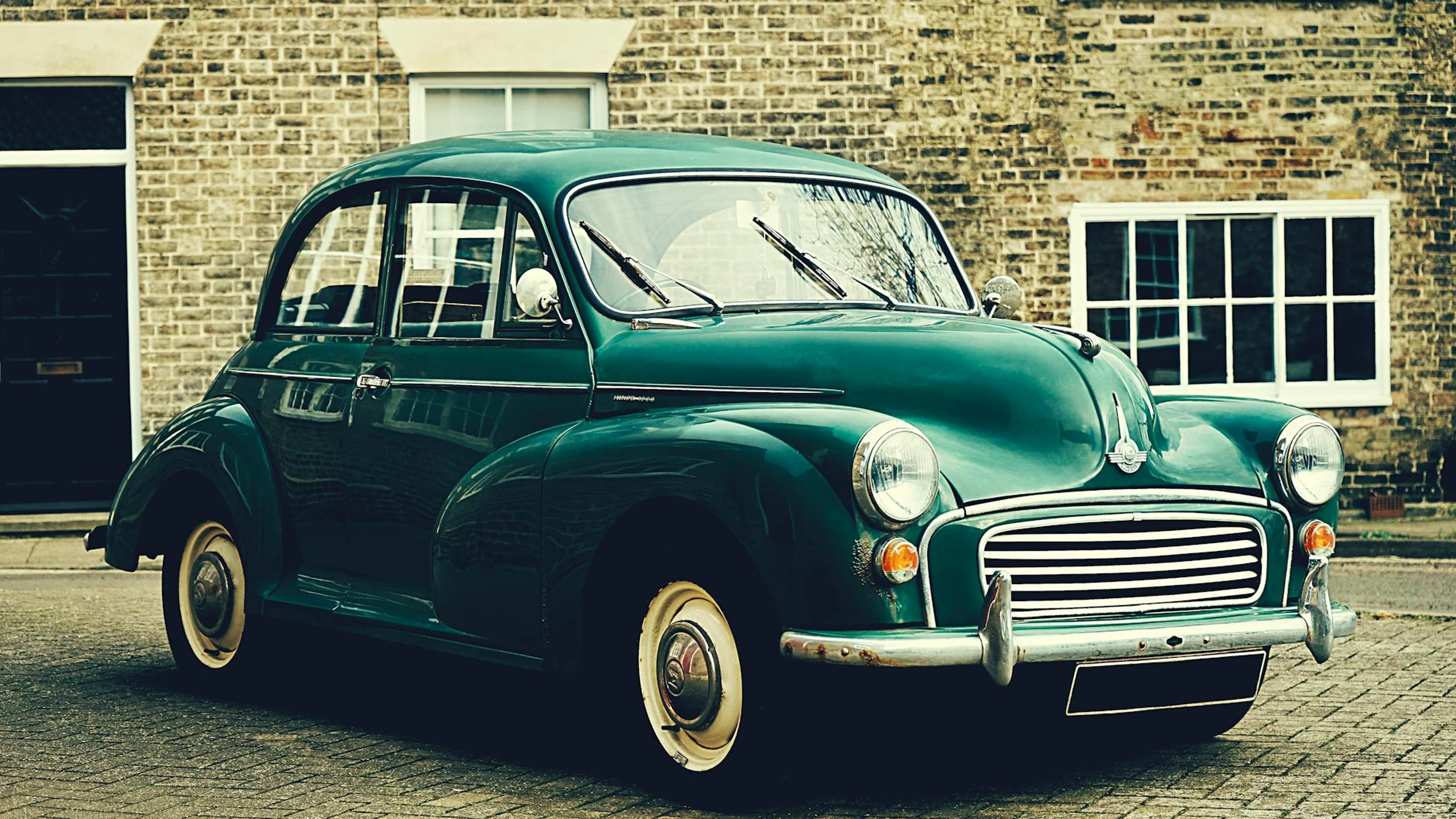 A classic Morris Minor parked outside a brick building in Ely, UK. Vintage charm - free 4K Ultra HD cars wallpaper for desktop