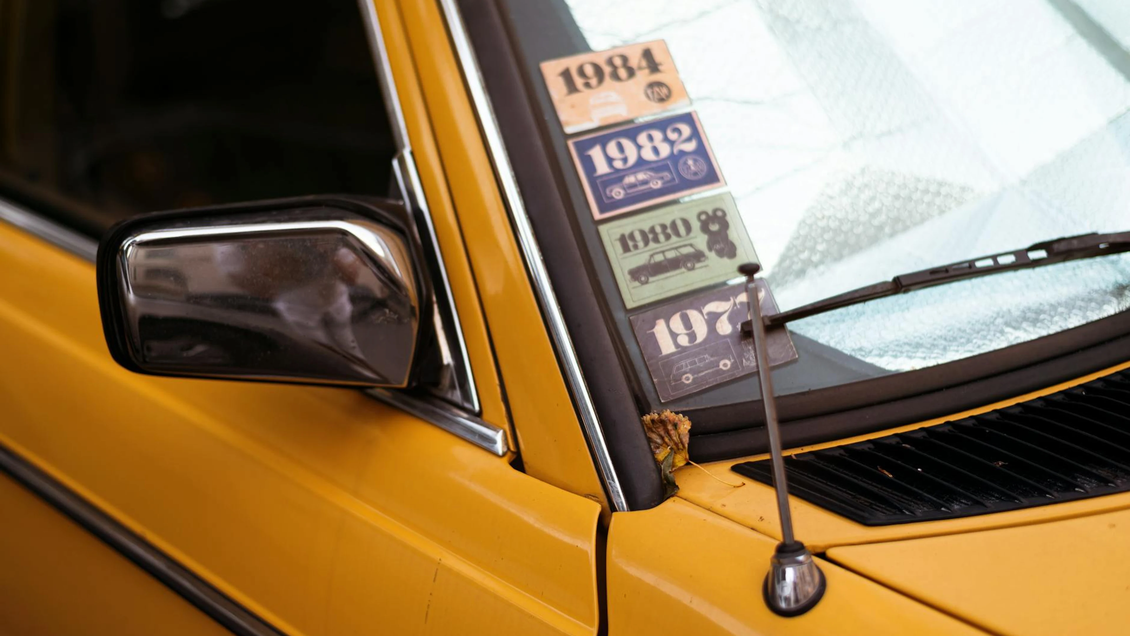 Close-up of a classic yellow car with retro decade stickers on the windshield. - free 4K Ultra HD cars wallpaper for desktop