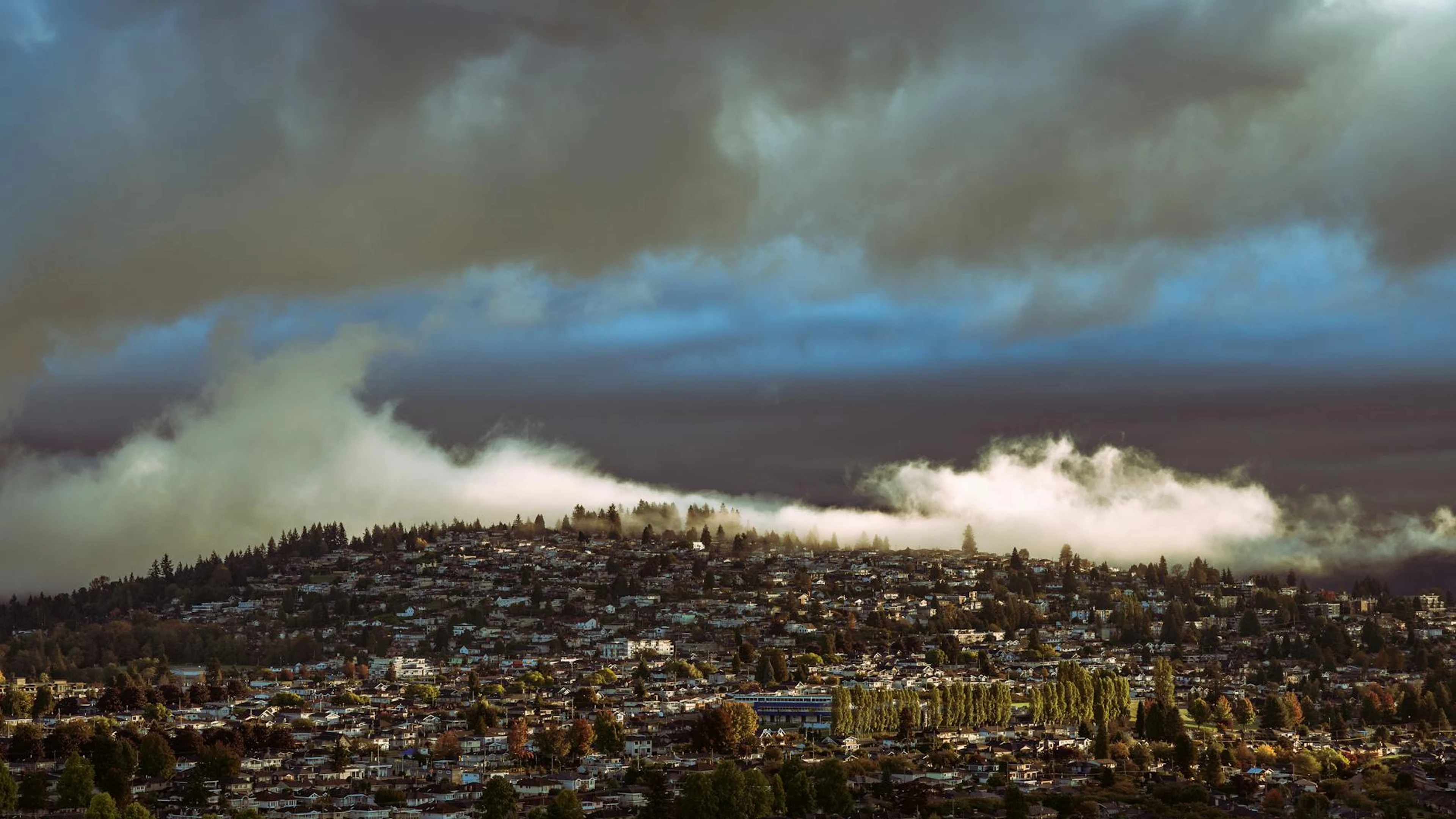 Aerial view of a cityscape under dramatic skies and clouds, showcasing a unique - free 4K Ultra HD city wallpaper for desktop