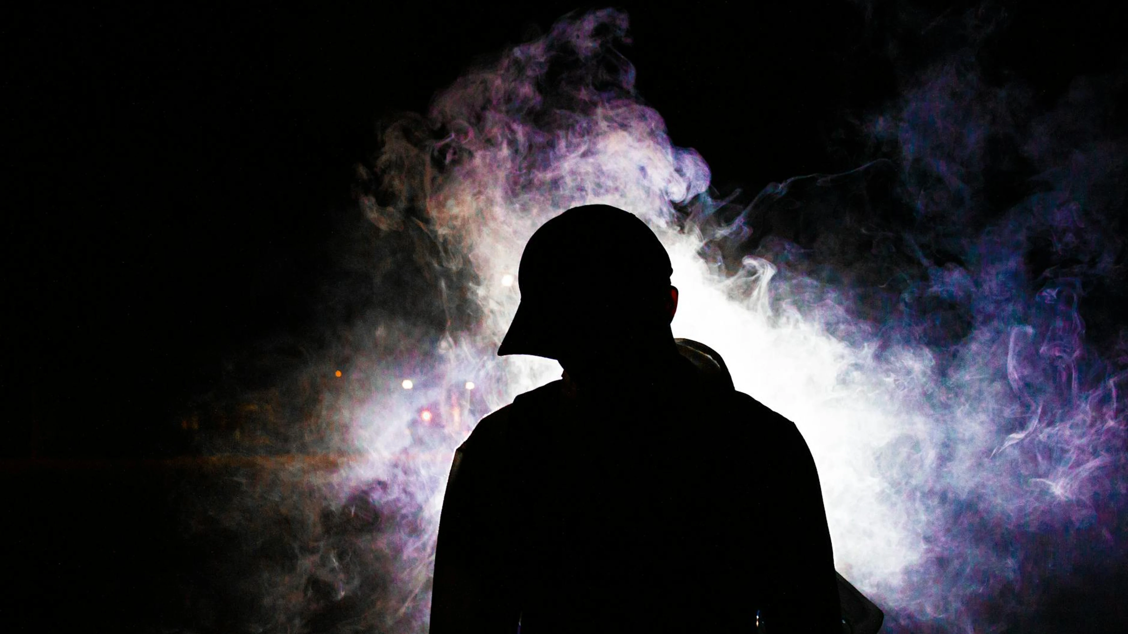 A dramatic silhouette of a man in a hoodie enveloped in backlit misty smoke, cre - free 4K Ultra HD dark wallpaper for desktop