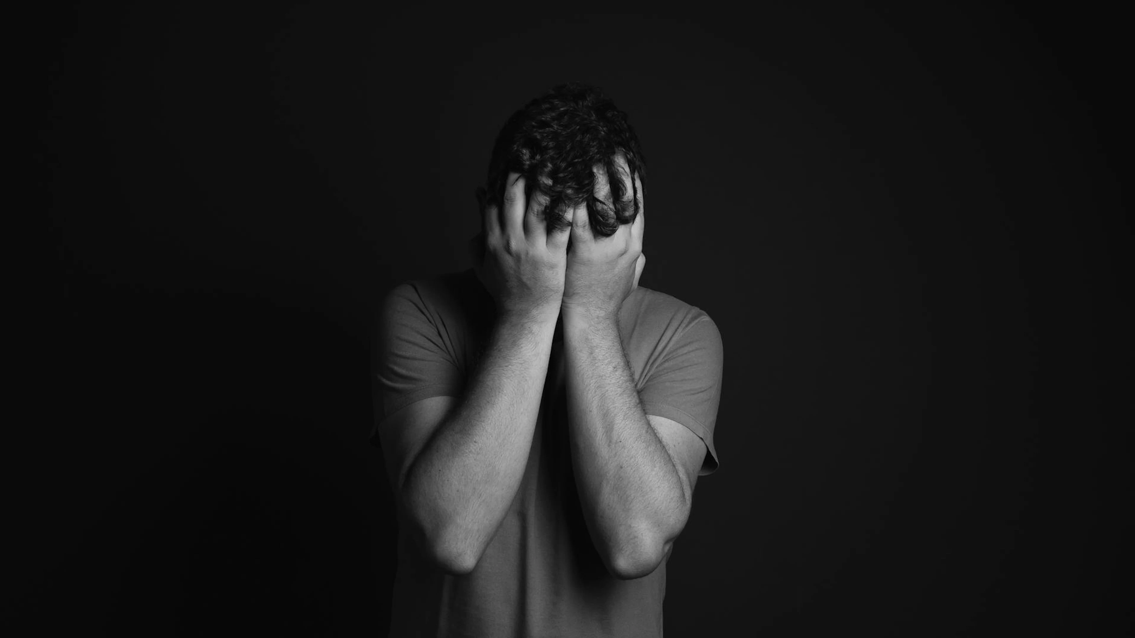 A grayscale portrait of a man covering his face, depicting emotion and mental he - free 4K Ultra HD dark wallpaper for desktop