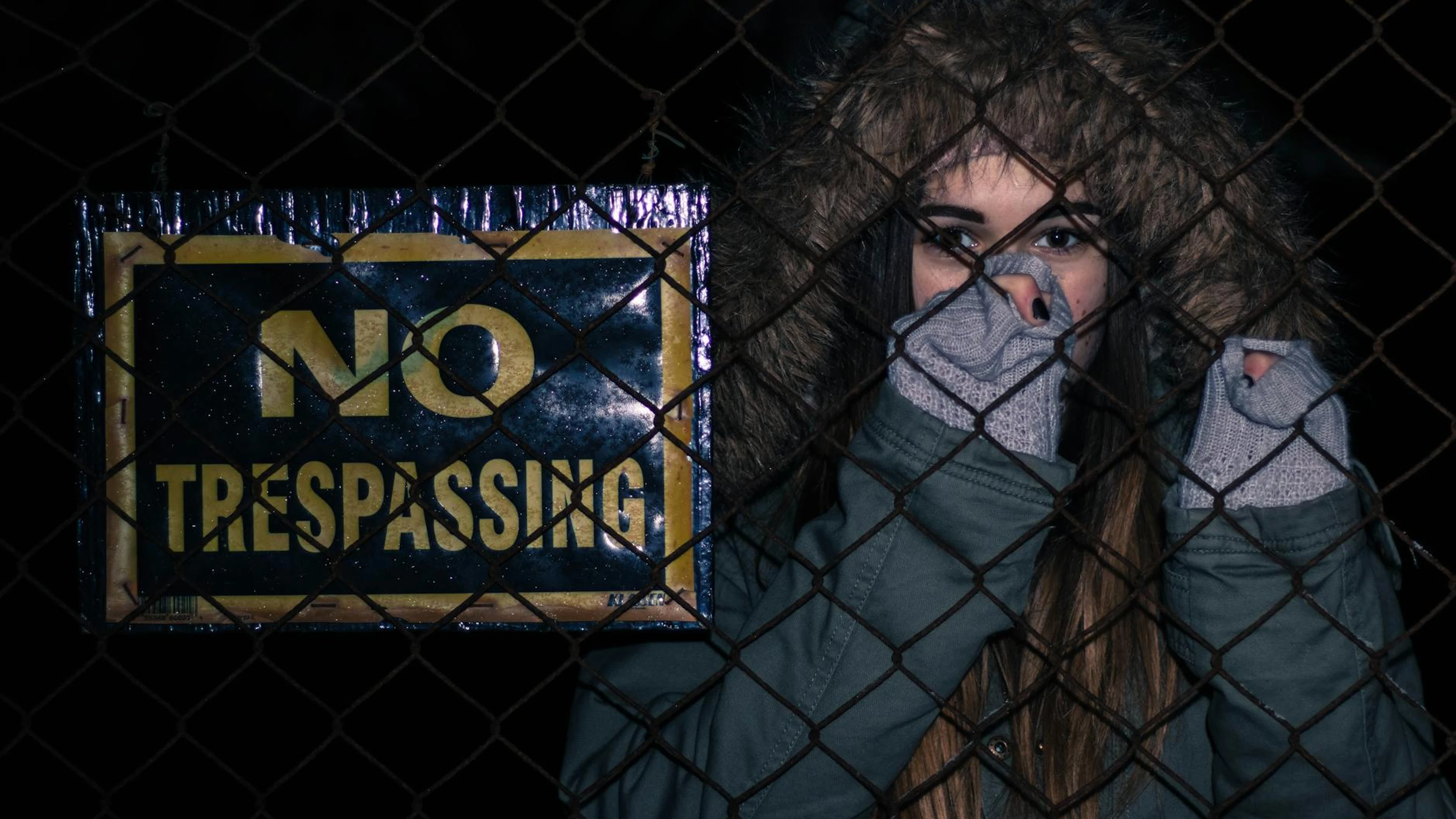 A woman in a hooded jacket stands behind a 'No Trespassing' sign, evoking myster - free 4K Ultra HD dark wallpaper for desktop