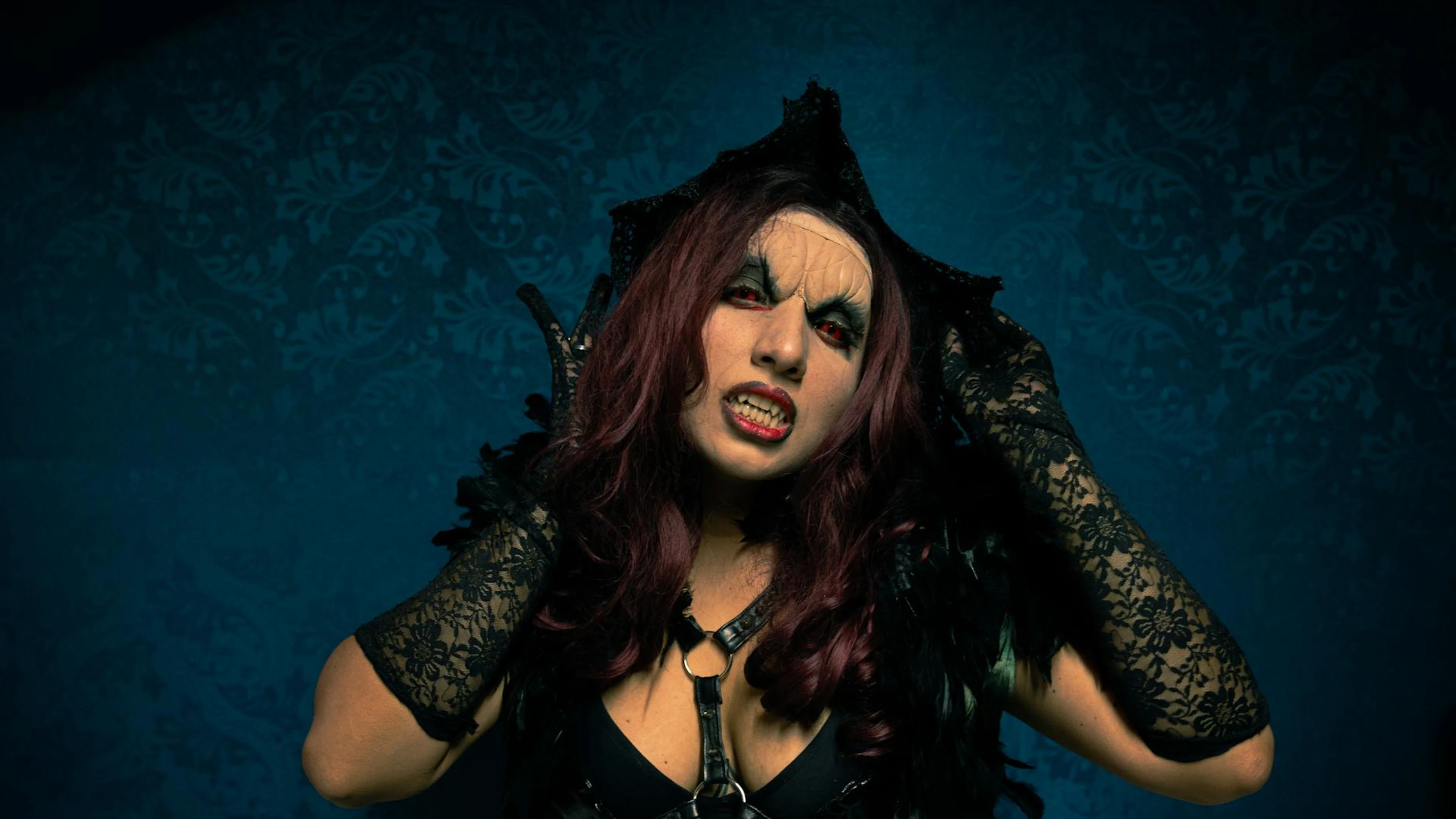 A woman in gothic attire poses against a patterned wall with bold makeup and lac - free 4K Ultra HD dark wallpaper for desktop