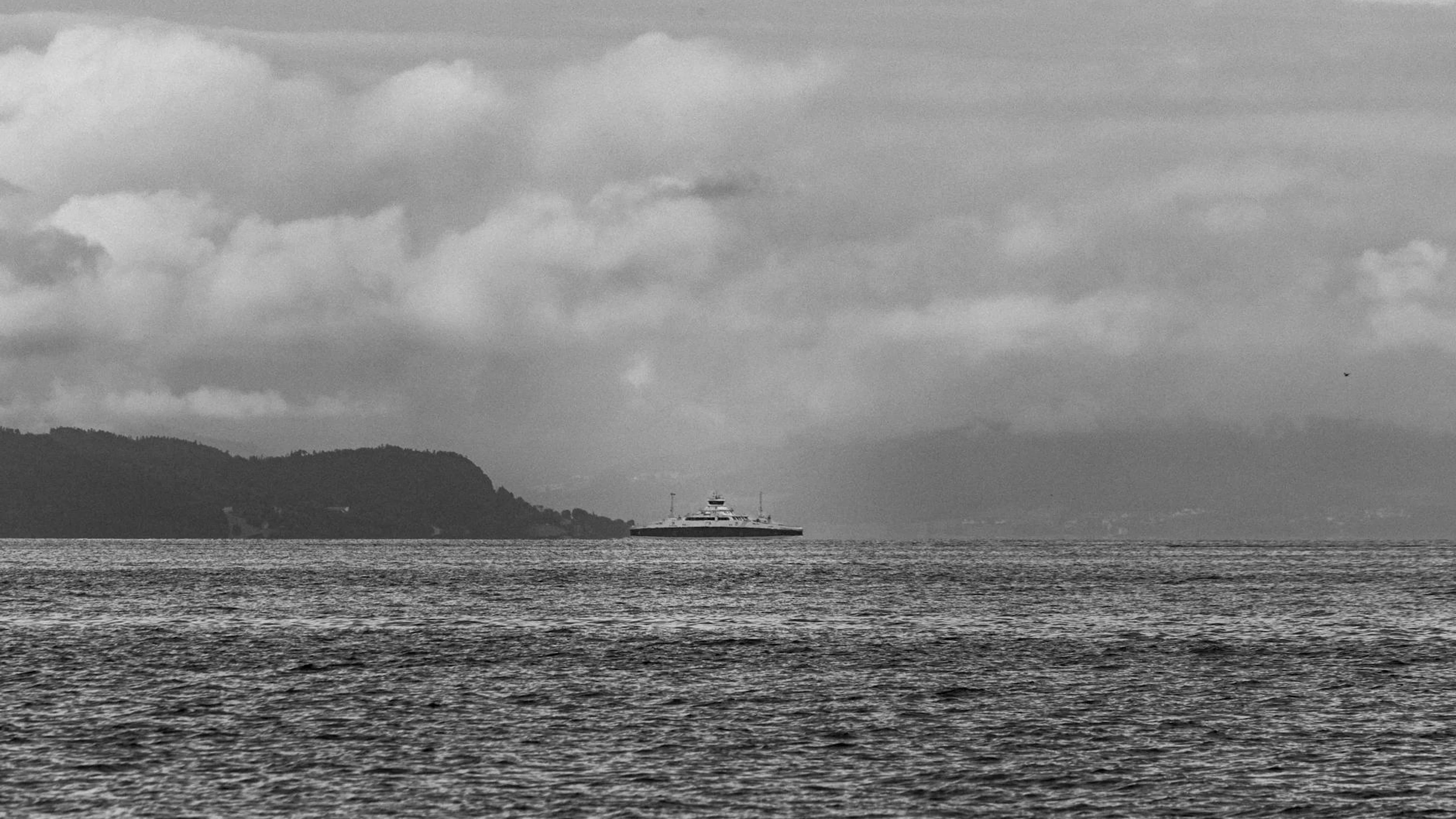 Dramatic black and white seascape with a solitary ship, cloudy sky, and distant - free 4K Ultra HD dark wallpaper for desktop