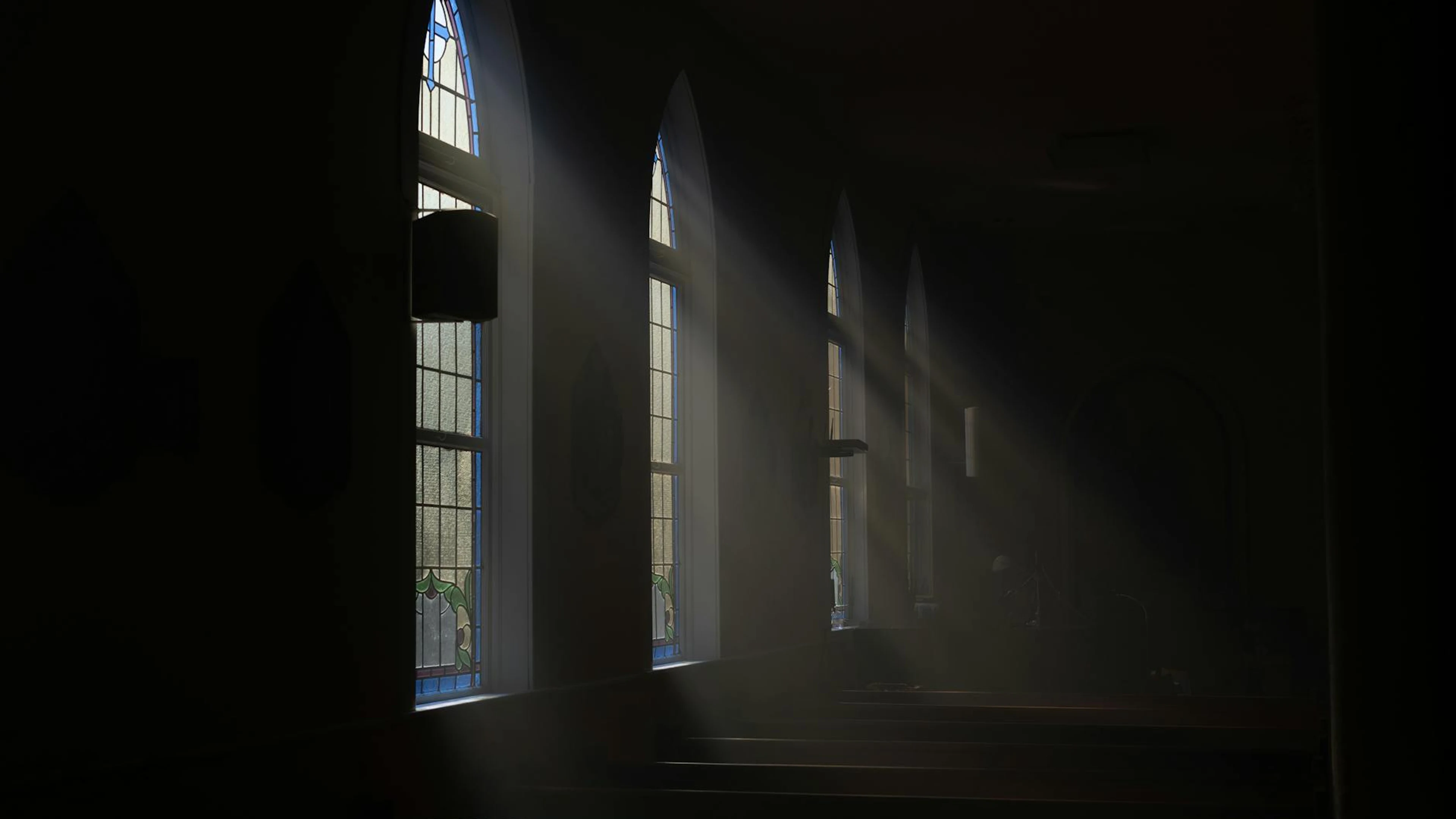 Dramatic light streams through arched windows, creating a mysterious atmosphere - free 4K Ultra HD dark wallpaper for desktop