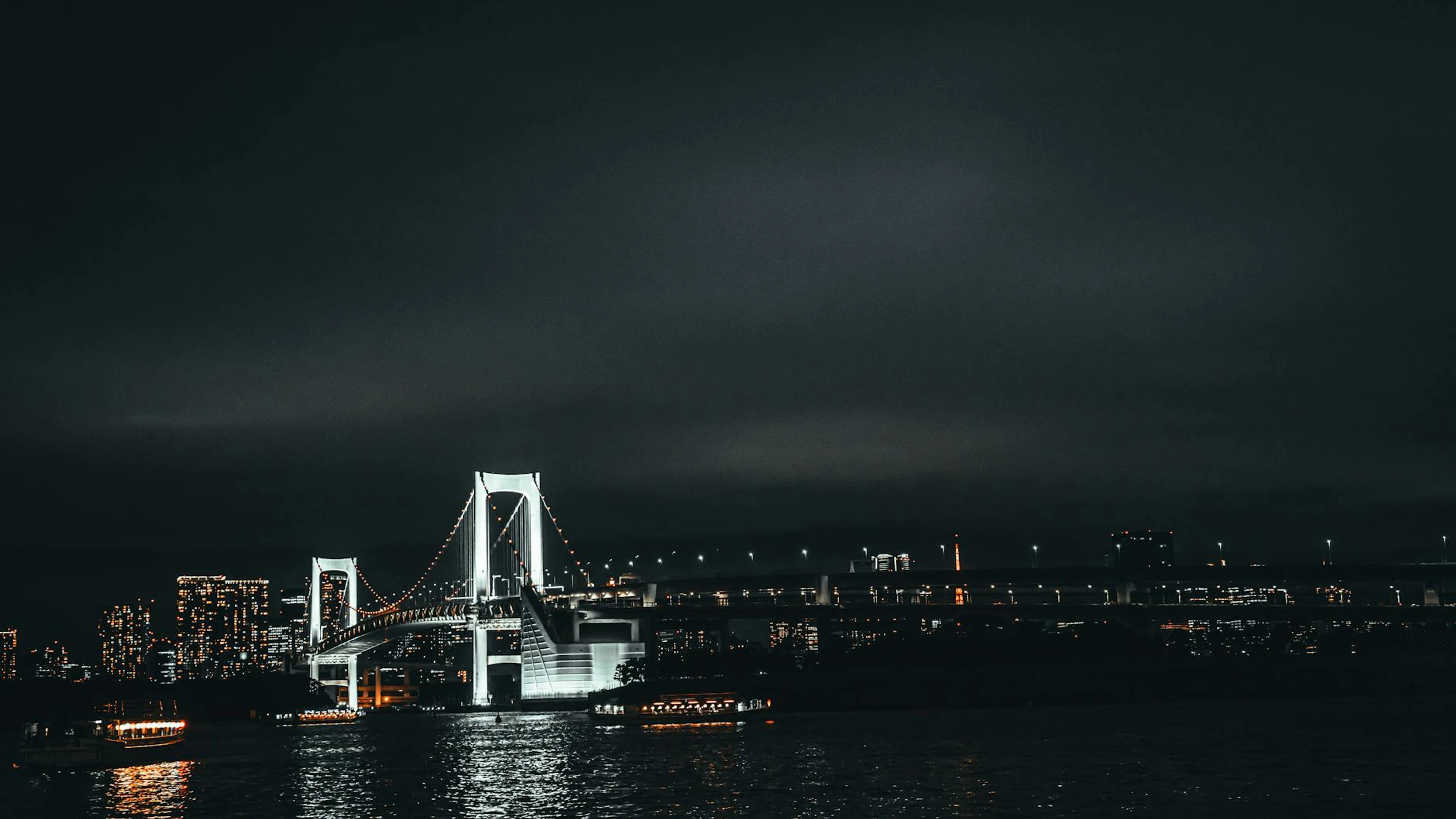 Stunning view of Tokyo's Rainbow Bridge at night, reflecting city lights over th - free 4K Ultra HD dark wallpaper for desktop
