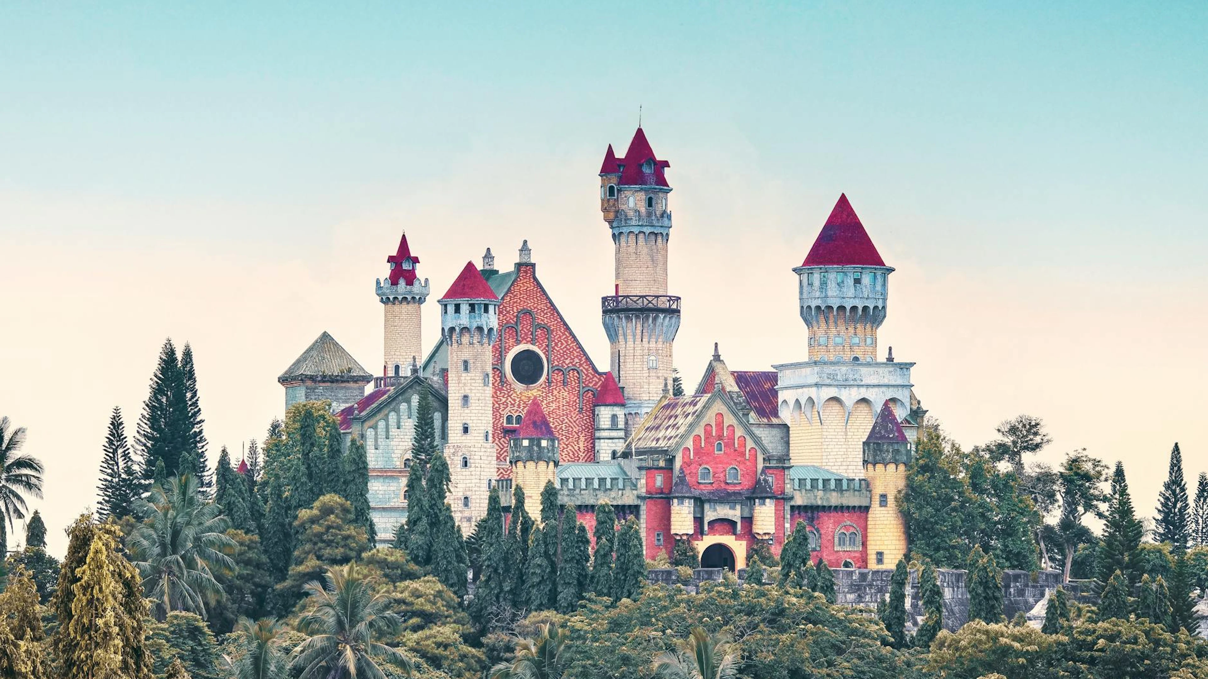 A colorful fairytale castle surrounded by lush trees under a clear blue sky. - free 4K Ultra HD fantasy wallpaper for desktop