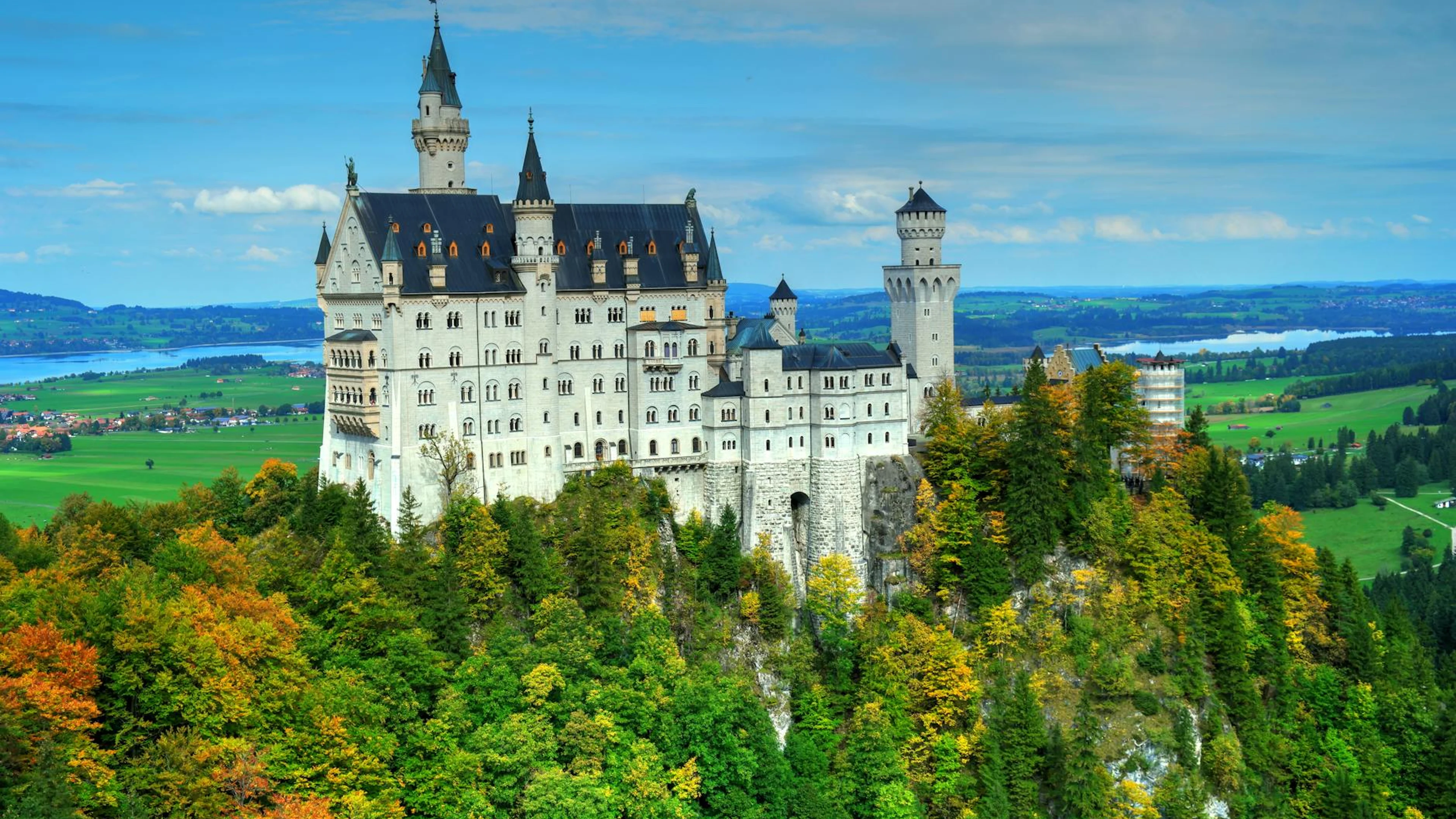 A scenic view of Neuschwanstein Castle surrounded by vibrant autumn foliage, set - free 4K Ultra HD fantasy wallpaper for desktop