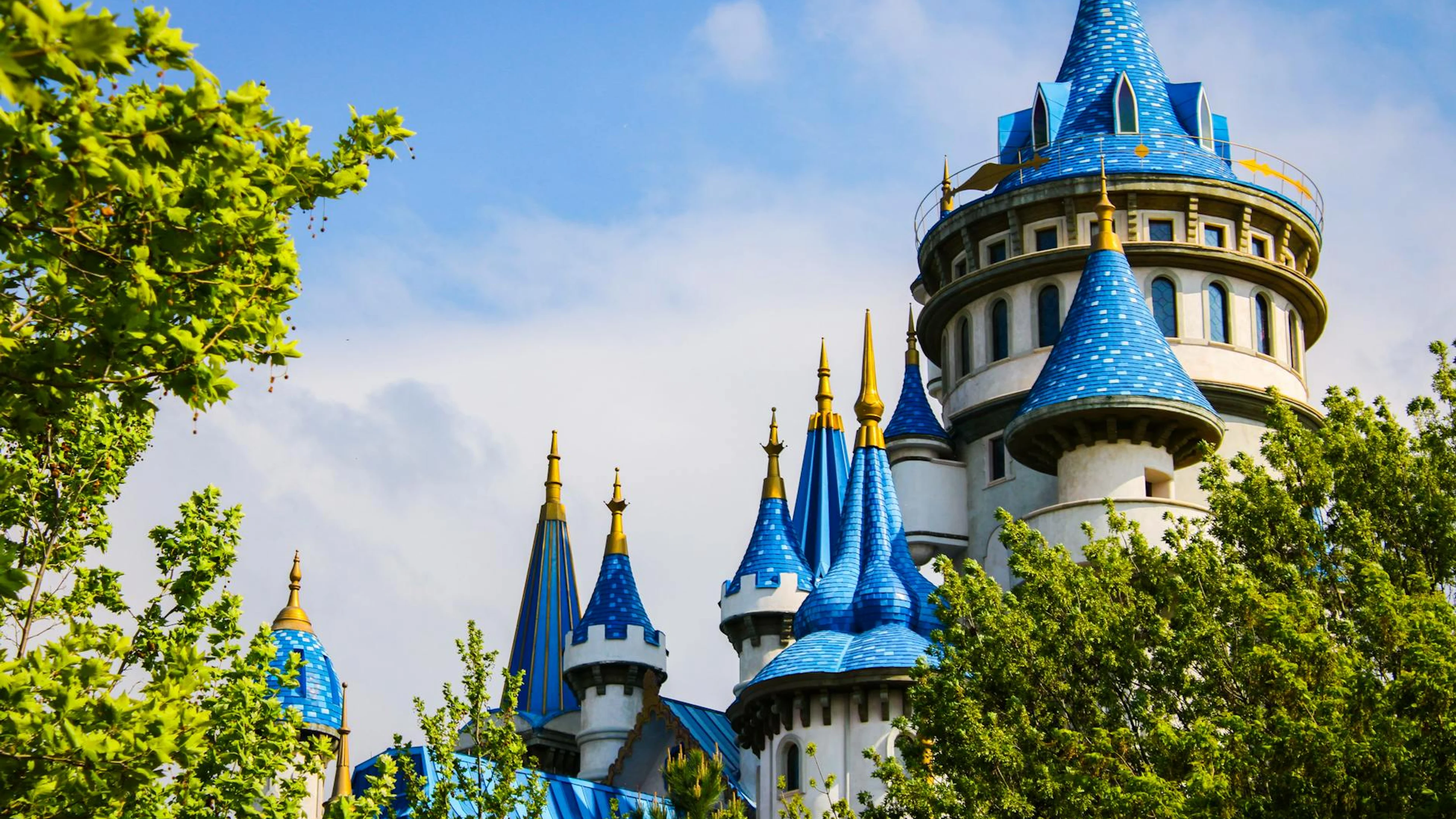 Stunning blue and white castle towers framed by vibrant greenery under a bright - free 4K Ultra HD fantasy wallpaper for desktop