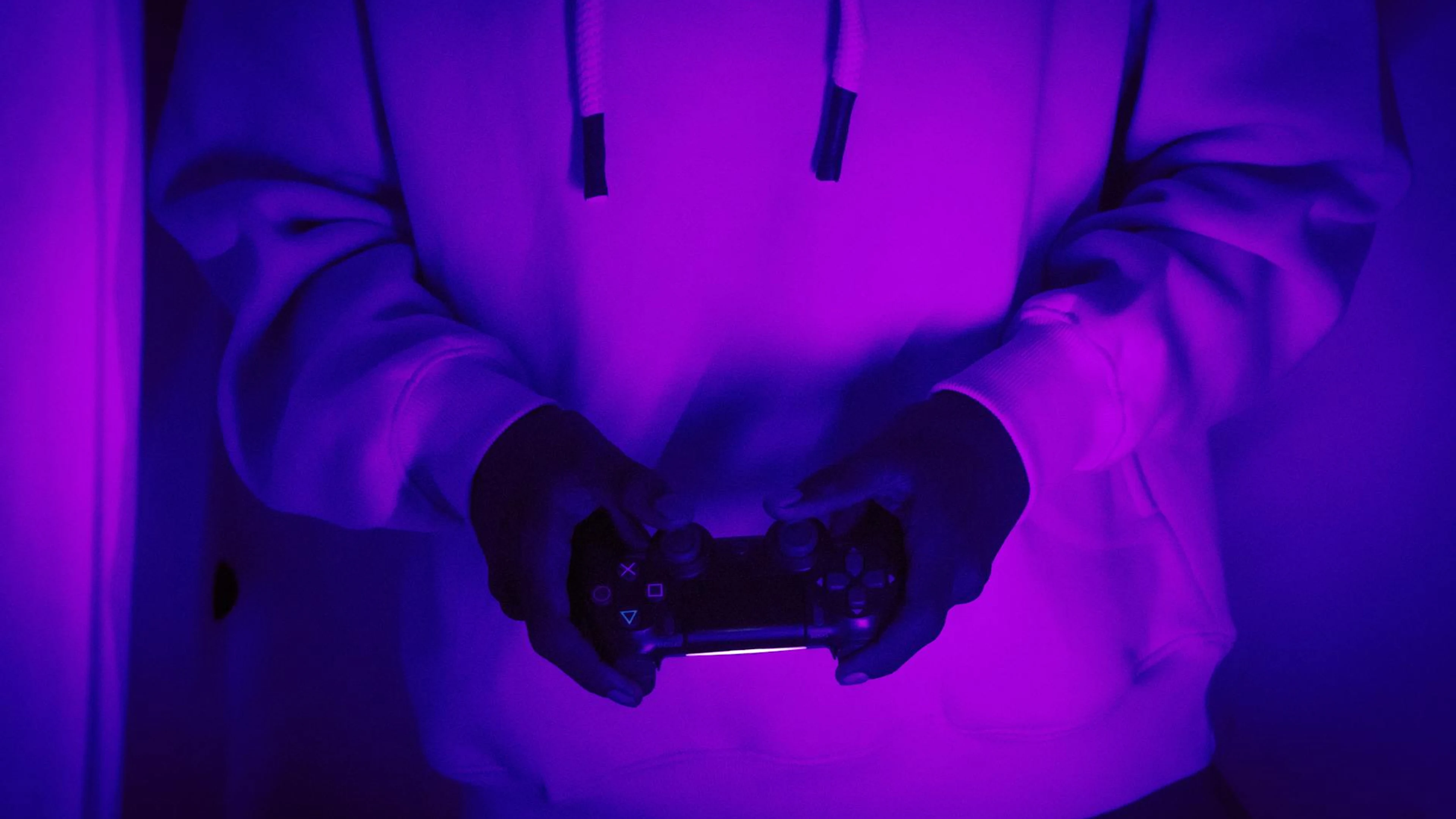 A person in a hoodie holds a game controller under neon purple light. - free 4K Ultra HD gaming wallpaper for desktop