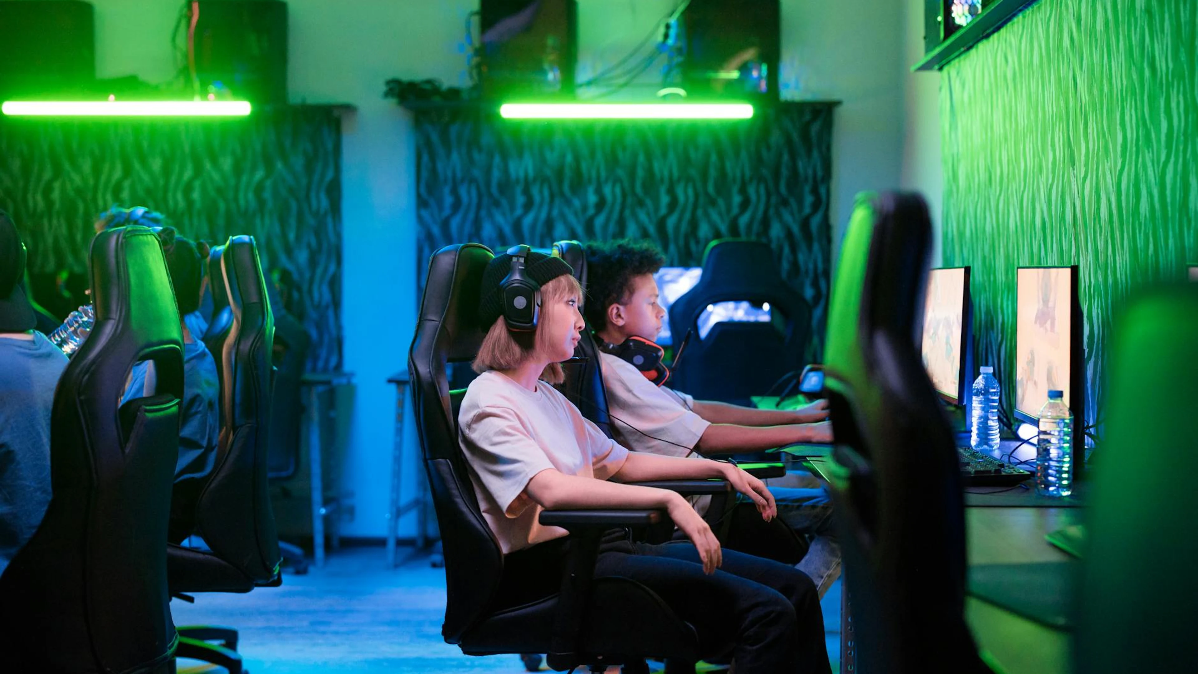 Teenagers immersed in online gaming in a neon-lit room, showcasing modern techno - free 4K Ultra HD gaming wallpaper for desktop