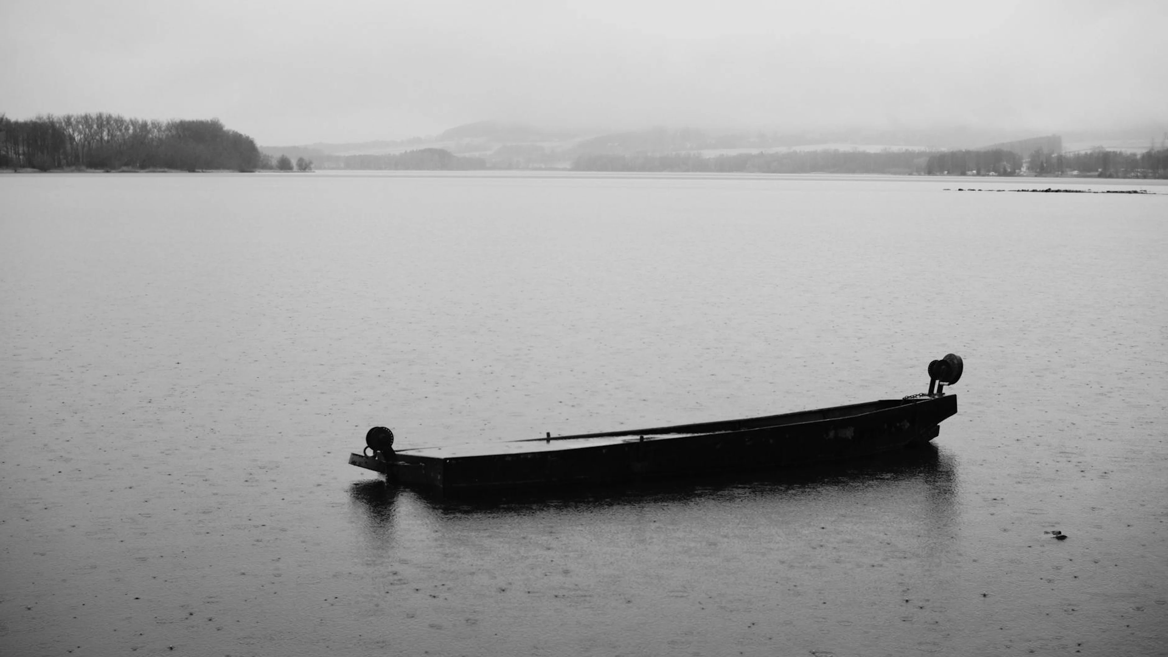 Monochrome image of a lone boat floating on a tranquil lake, evoking solitude. - free 4K Ultra HD lake wallpaper for desktop
