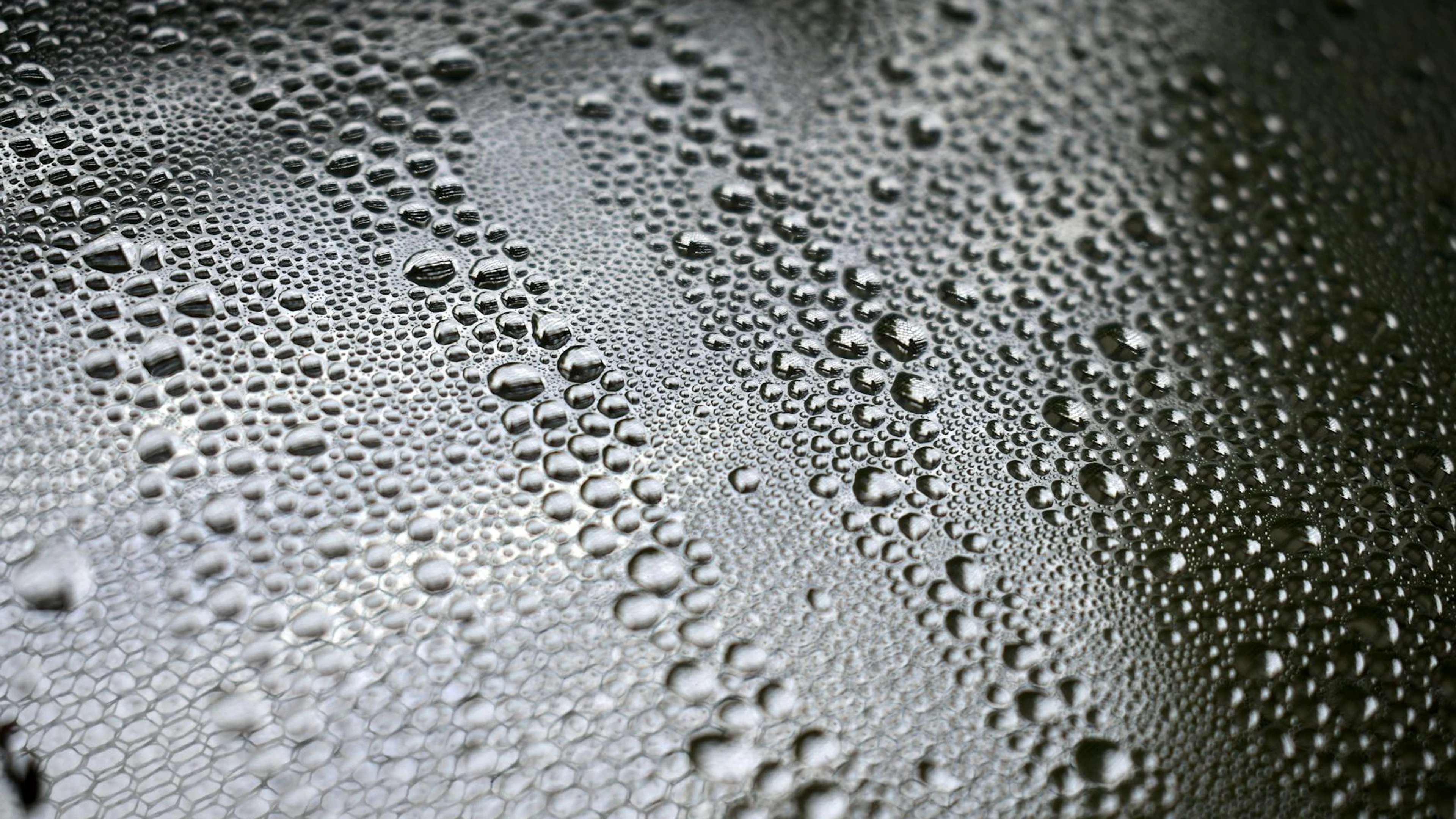 Detailed close-up of water droplets forming patterns on a black surface, showcas - free 4K Ultra HD macro wallpaper for desktop
