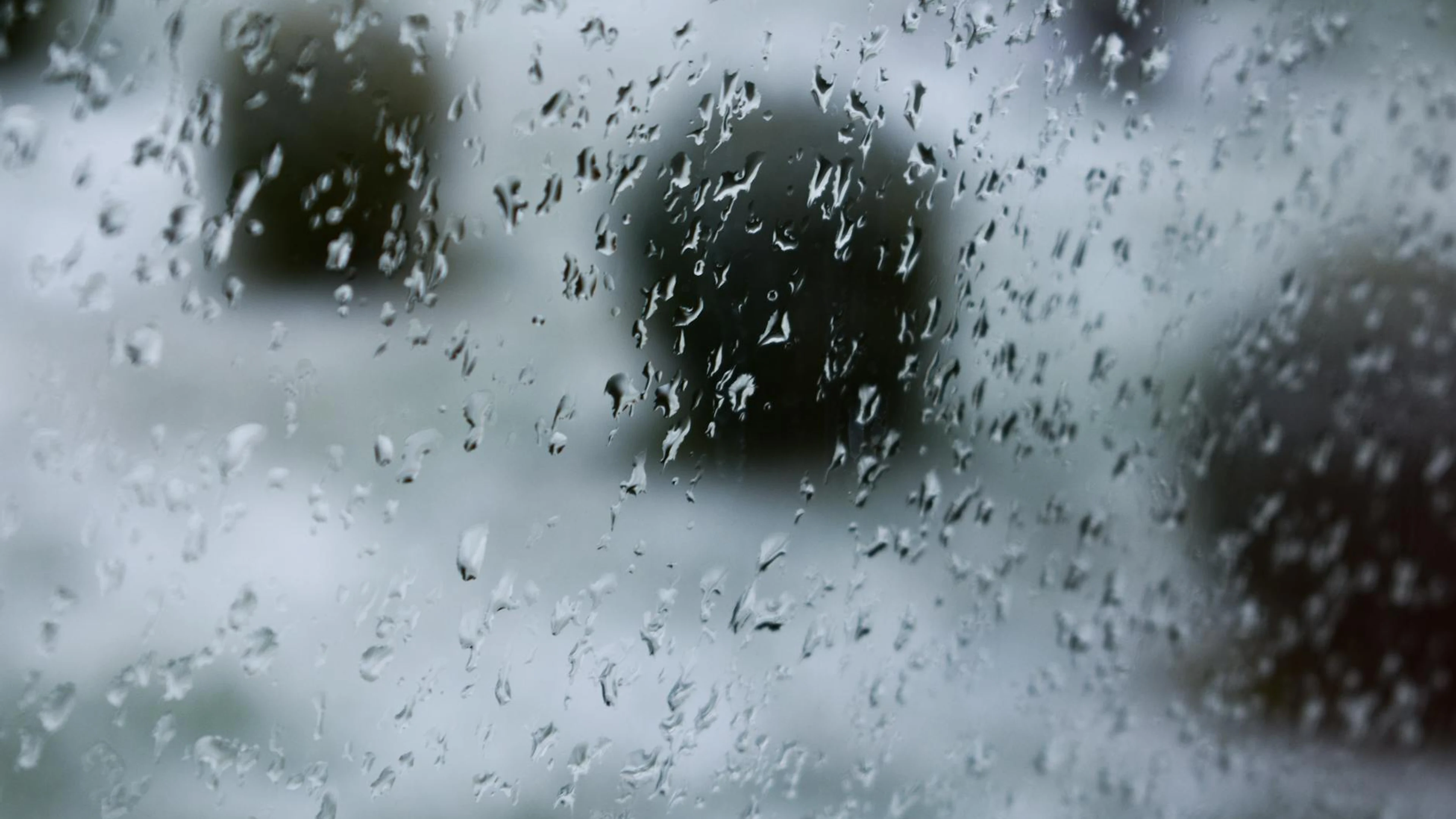 Raindrops on a glass window with a blurred outdoors background, creating an abst - free 4K Ultra HD macro wallpaper for desktop