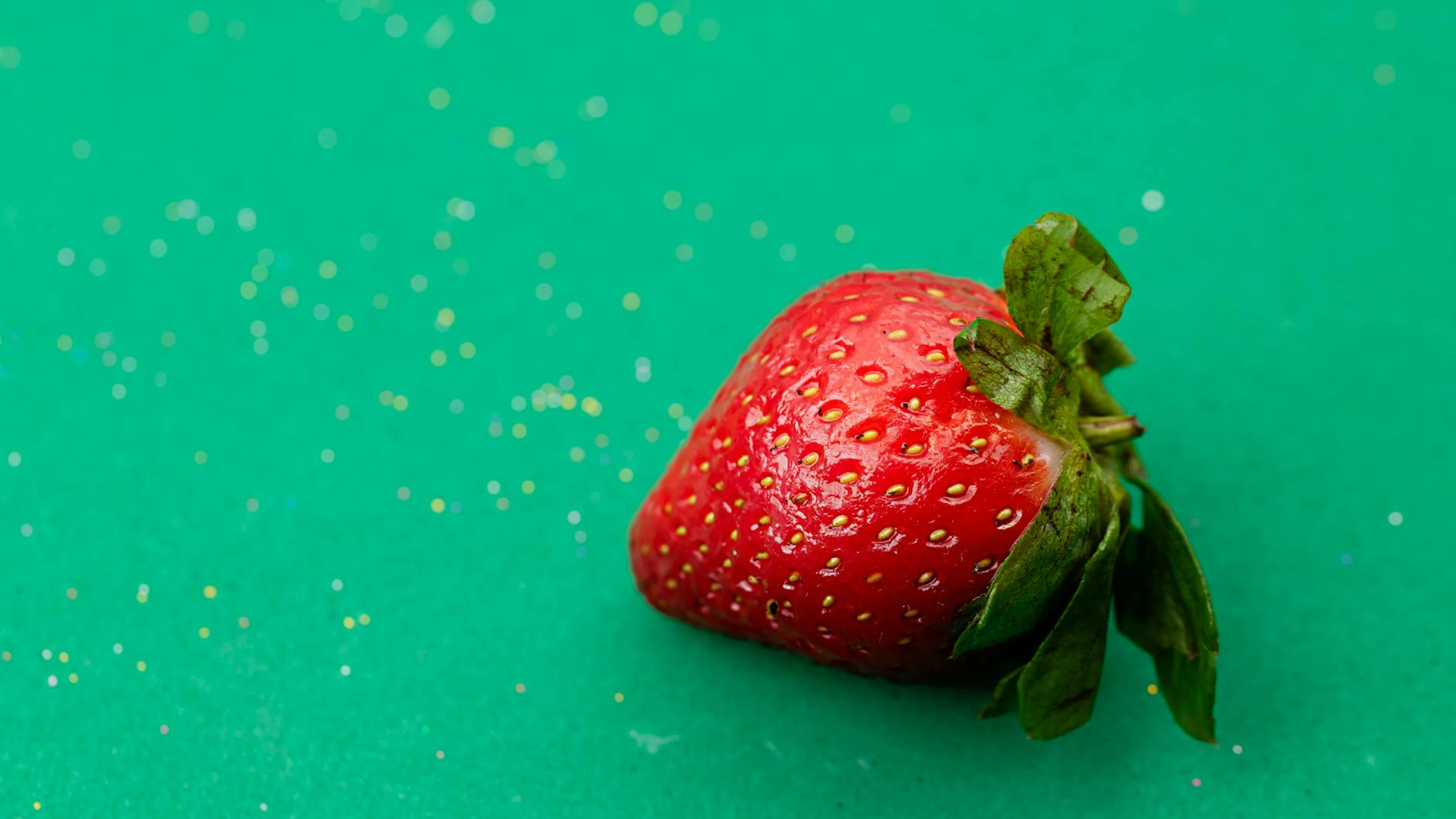 Close-up of a ripe, juicy strawberry on a sparkling green surface, exuding fresh - free 4K Ultra HD minimal wallpaper for desktop