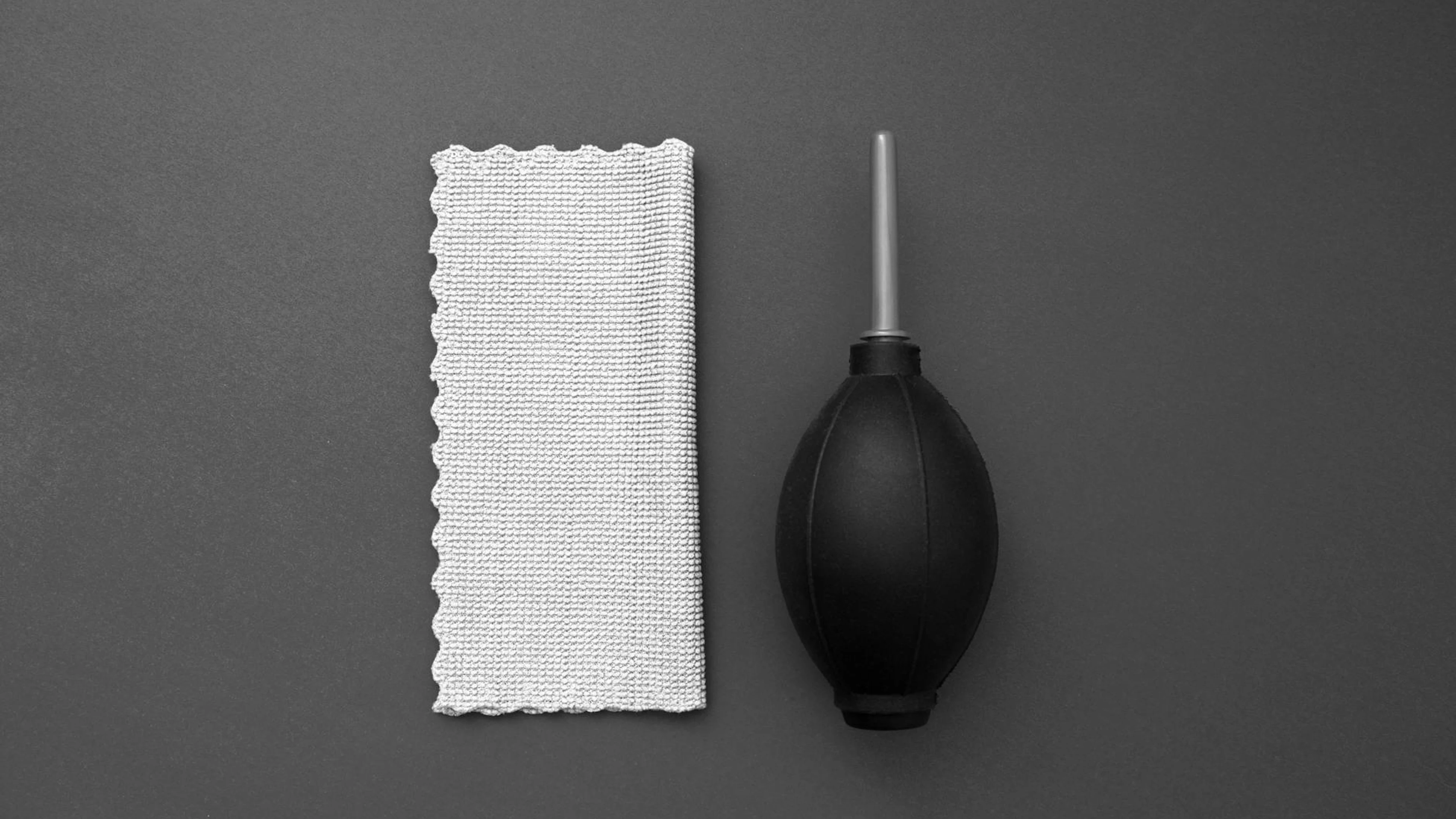 Overhead view of a camera cleaning blower and microfiber cloth on a gray backgro - free 4K Ultra HD minimal wallpaper for desktop