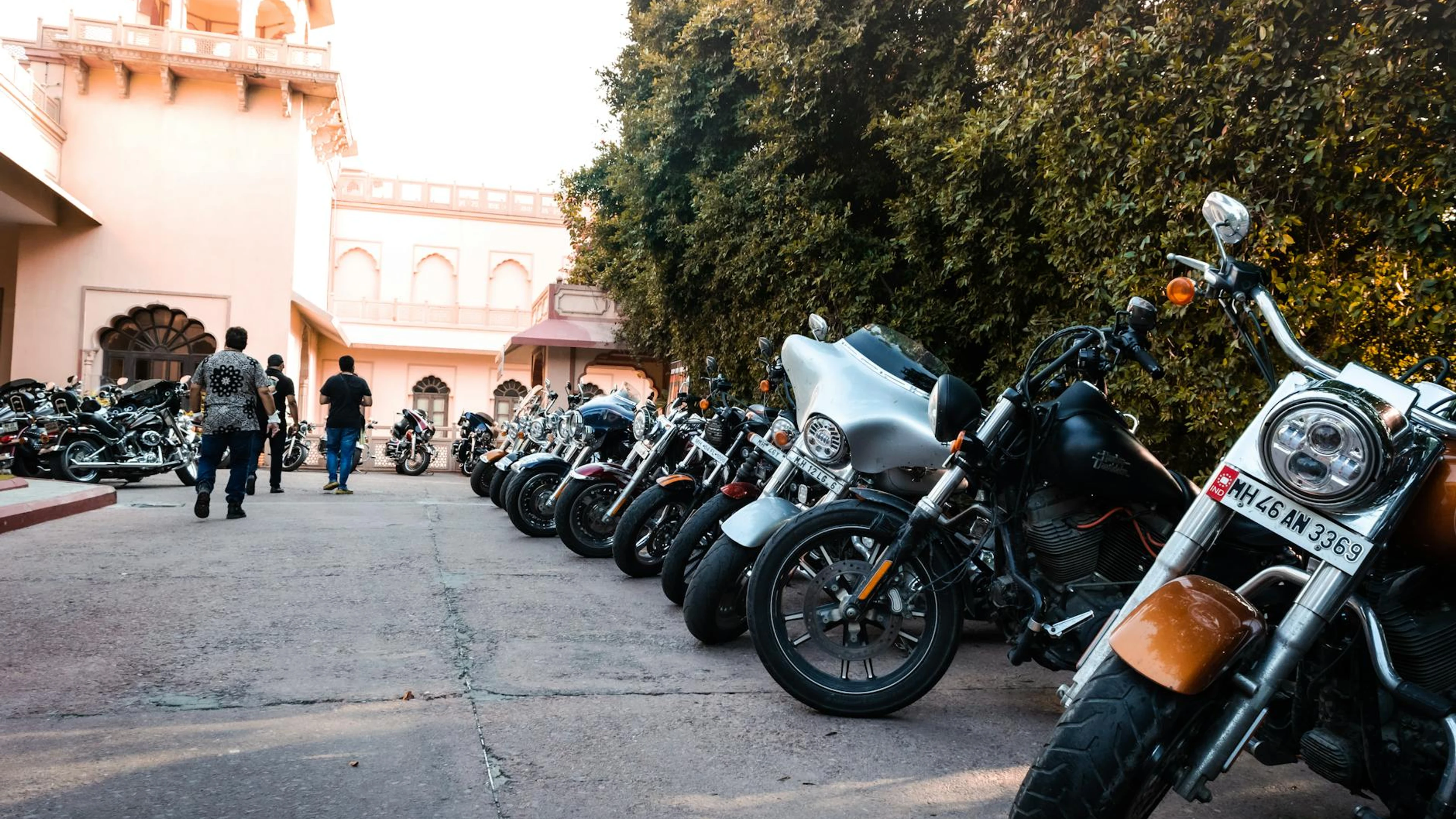 A row of motorcycles parked outside a historic building with trees and people wa - free 4K Ultra HD motorcycle wallpaper for desktop