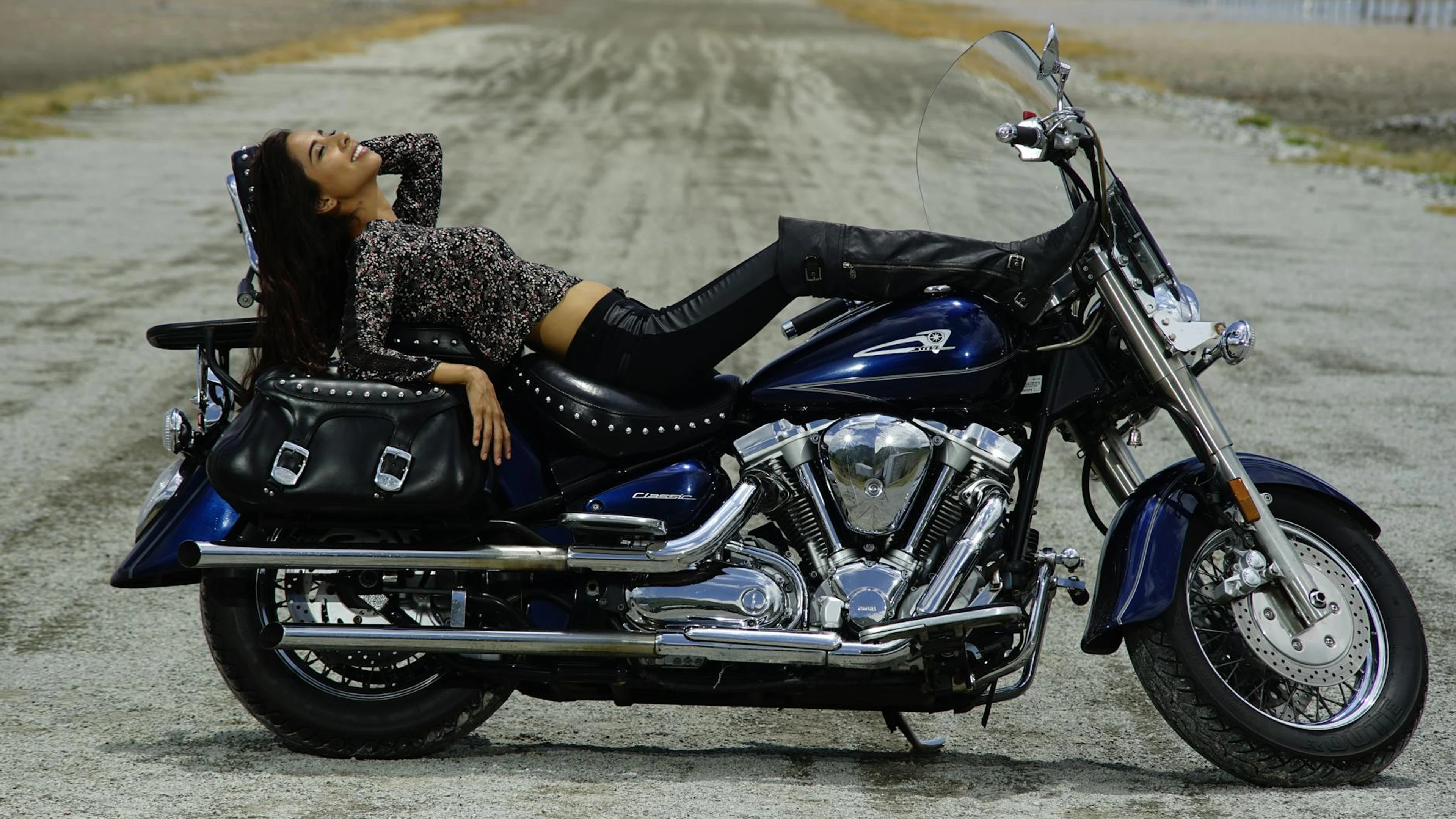 A woman lying on a parked motorcycle on a remote rural road, enjoying a carefree - free 4K Ultra HD motorcycle wallpaper for desktop