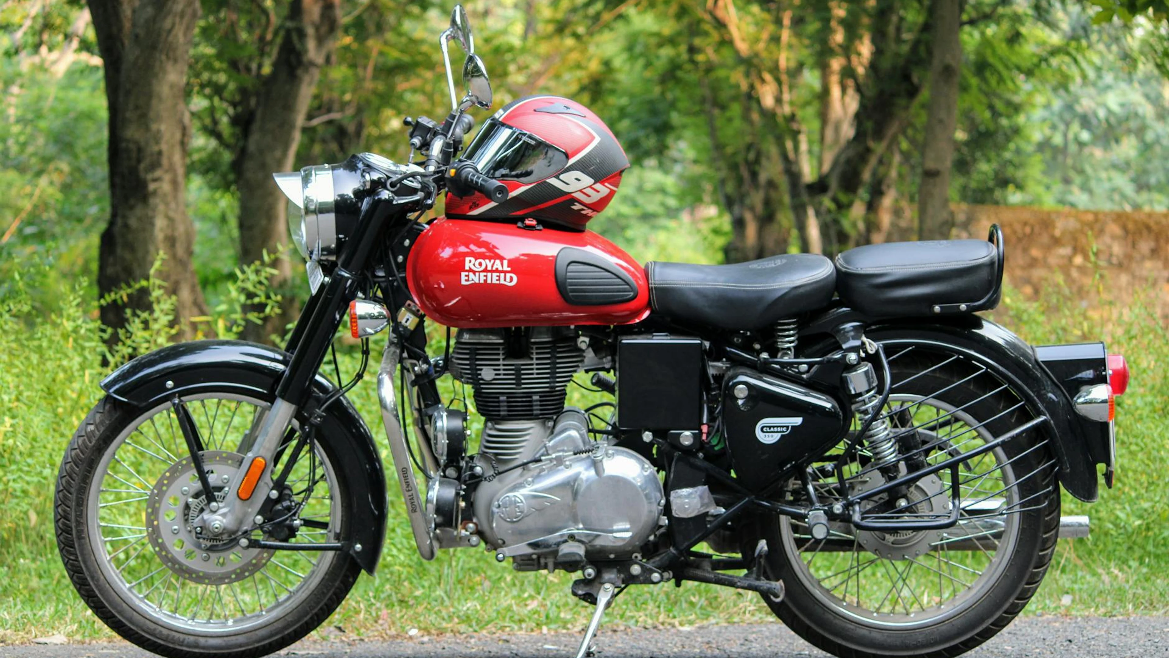Classic Royal Enfield motorcycle parked on a scenic outdoor road with helmet. - free 4K Ultra HD motorcycle wallpaper for desktop