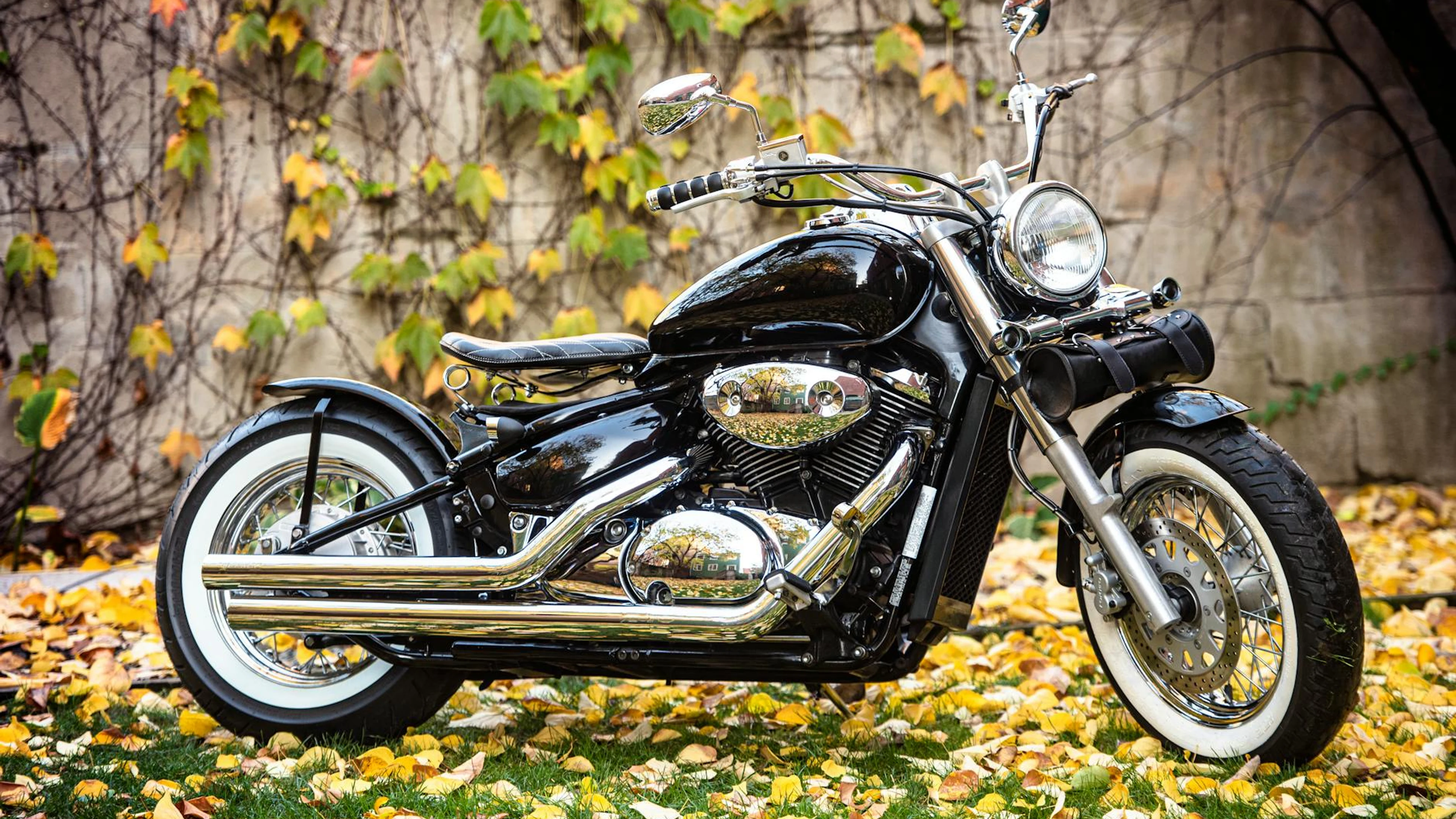 Classic vintage motorcycle parked on fallen autumn leaves with ivy-covered wall - free 4K Ultra HD motorcycle wallpaper for desktop