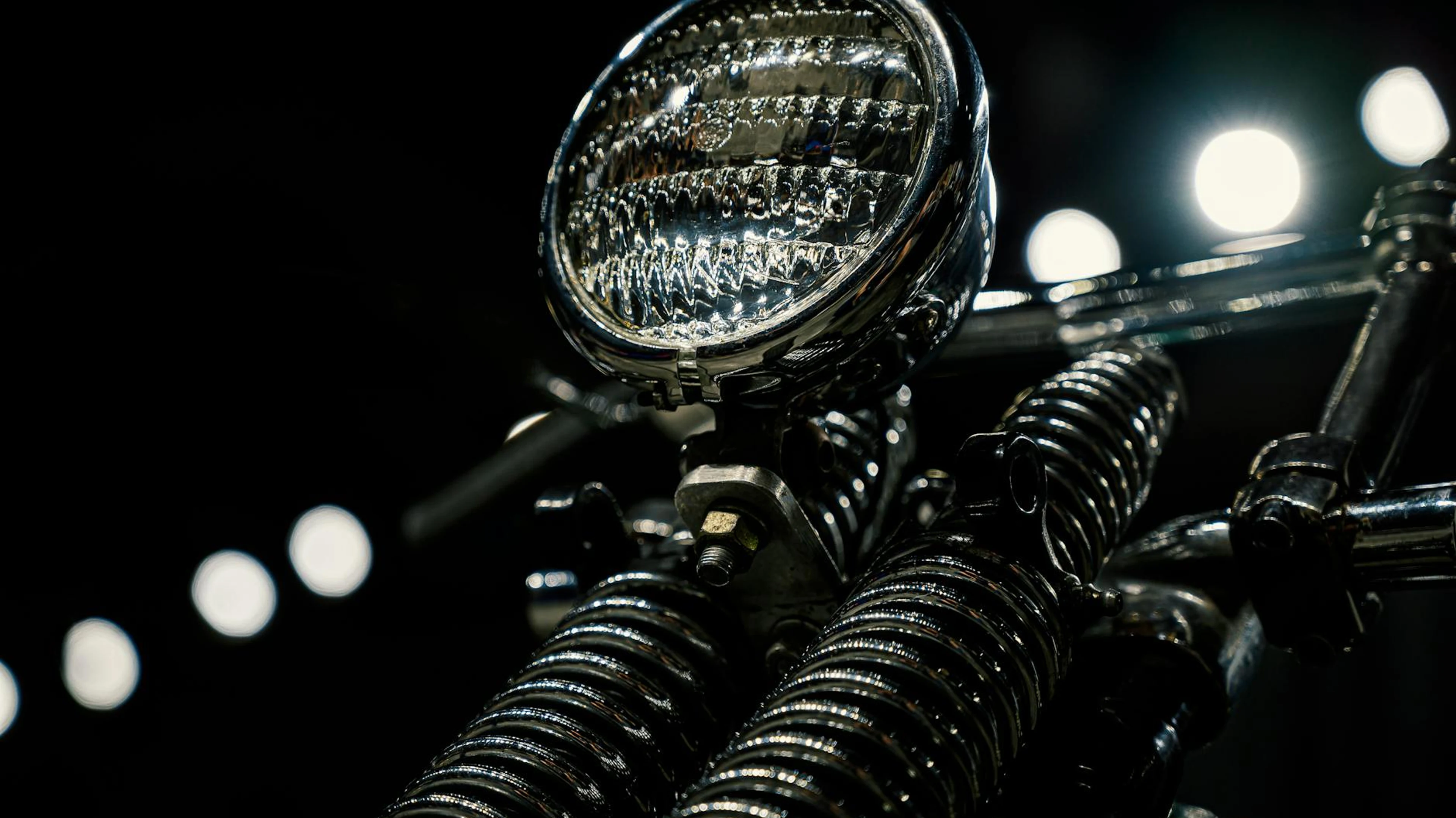 Close-up of a vintage motorcycle headlight with chrome detailing in low light. - free 4K Ultra HD motorcycle wallpaper for desktop