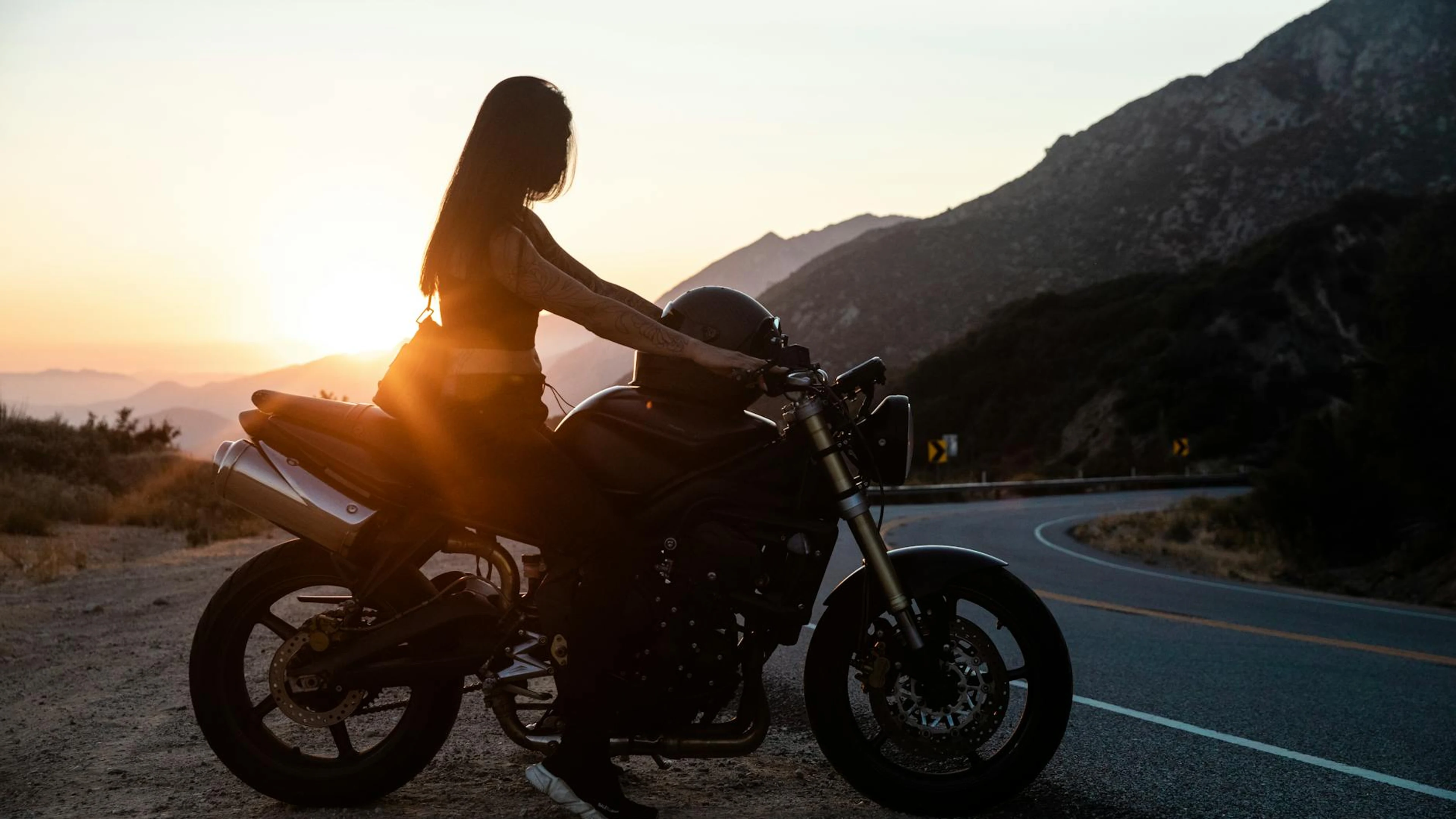 Woman on a motorcycle at sunset on a scenic mountain road. - free 4K Ultra HD motorcycle wallpaper for desktop
