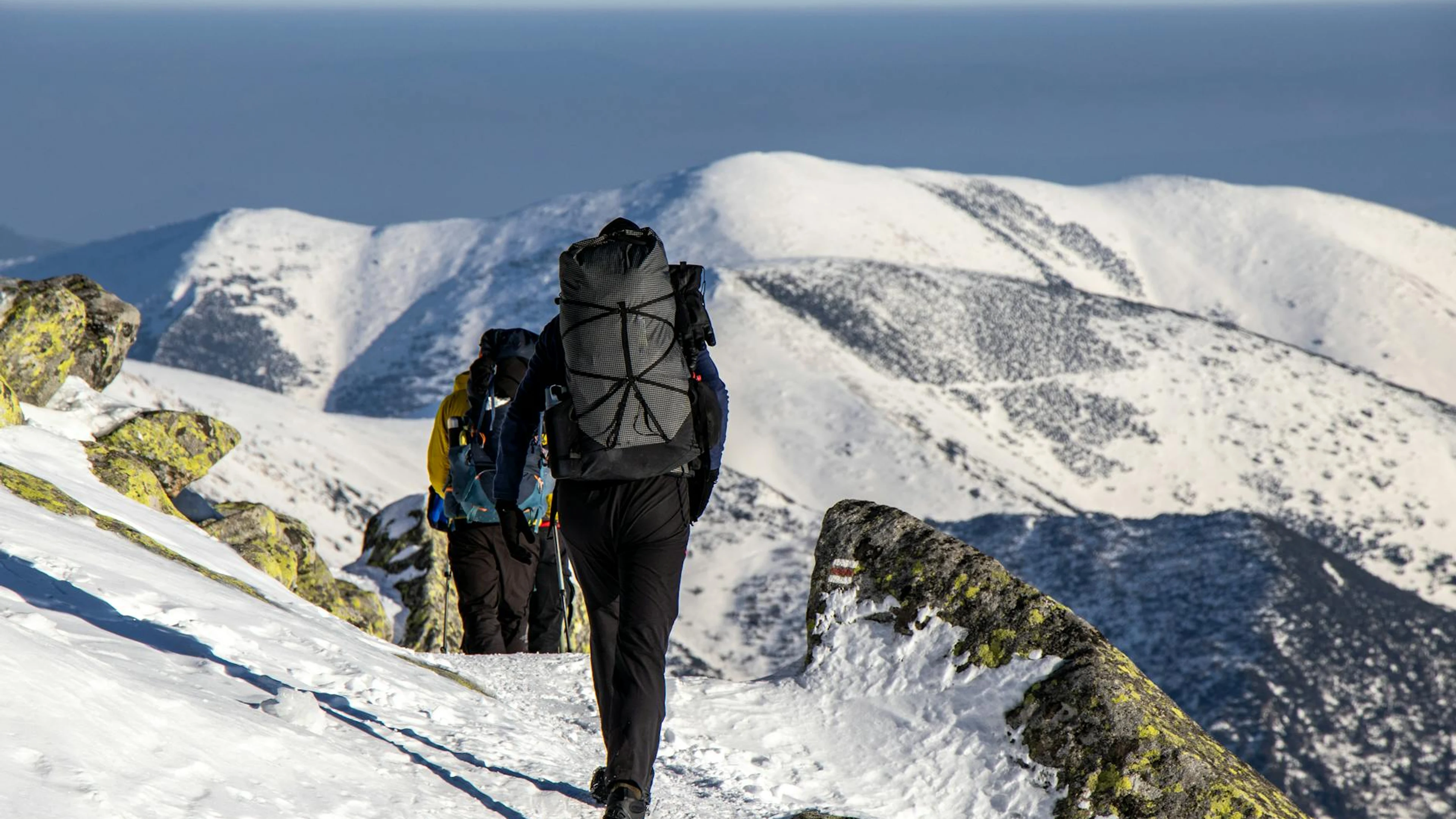 Hikers with backpacks trek through snow-covered mountains on a sunny winter day. - free 4K Ultra HD mountain wallpaper for desktop