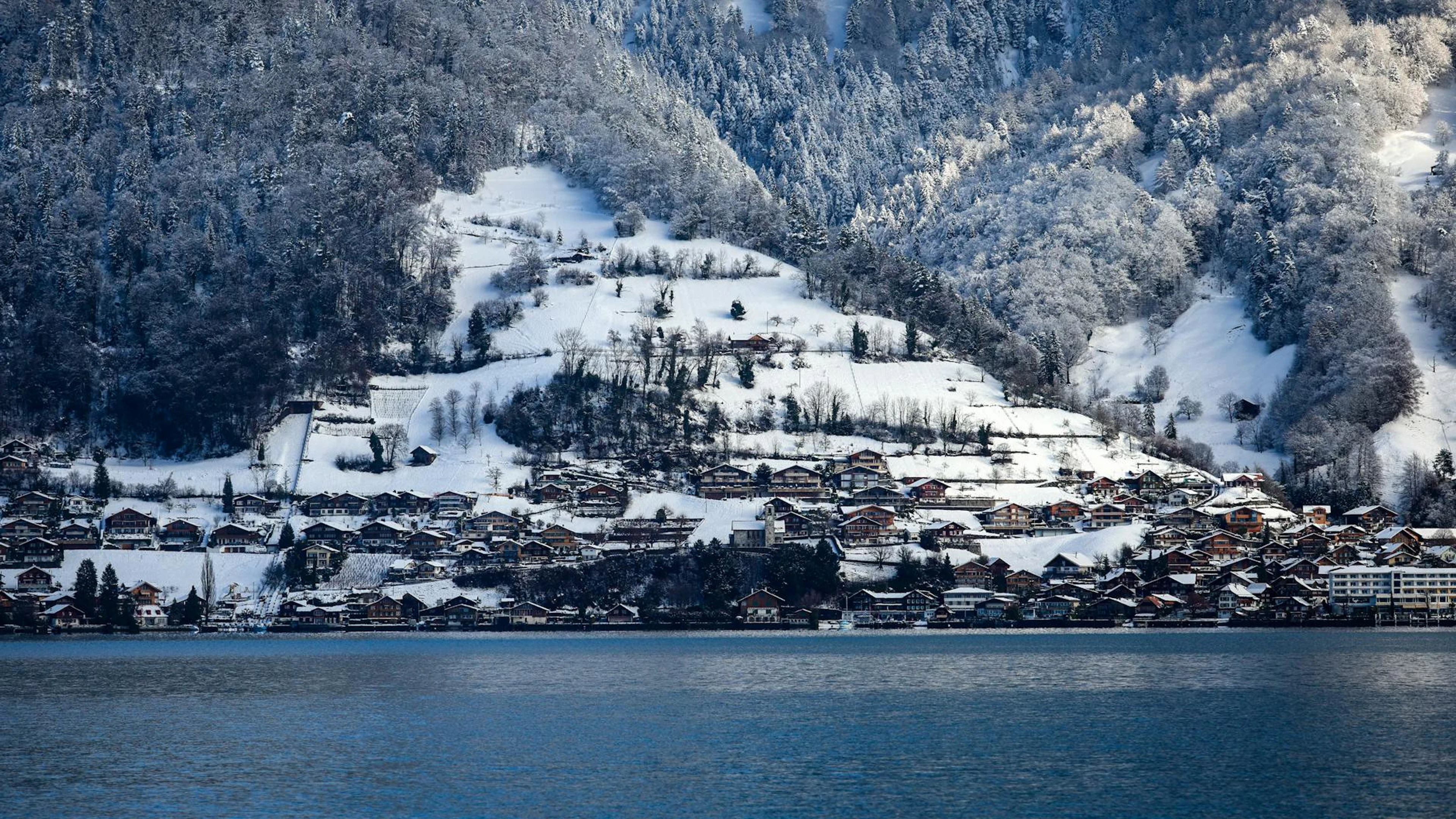 Peaceful snowy Swiss village nestled by a serene lake with scenic mountain backd - free 4K Ultra HD mountain wallpaper for desktop