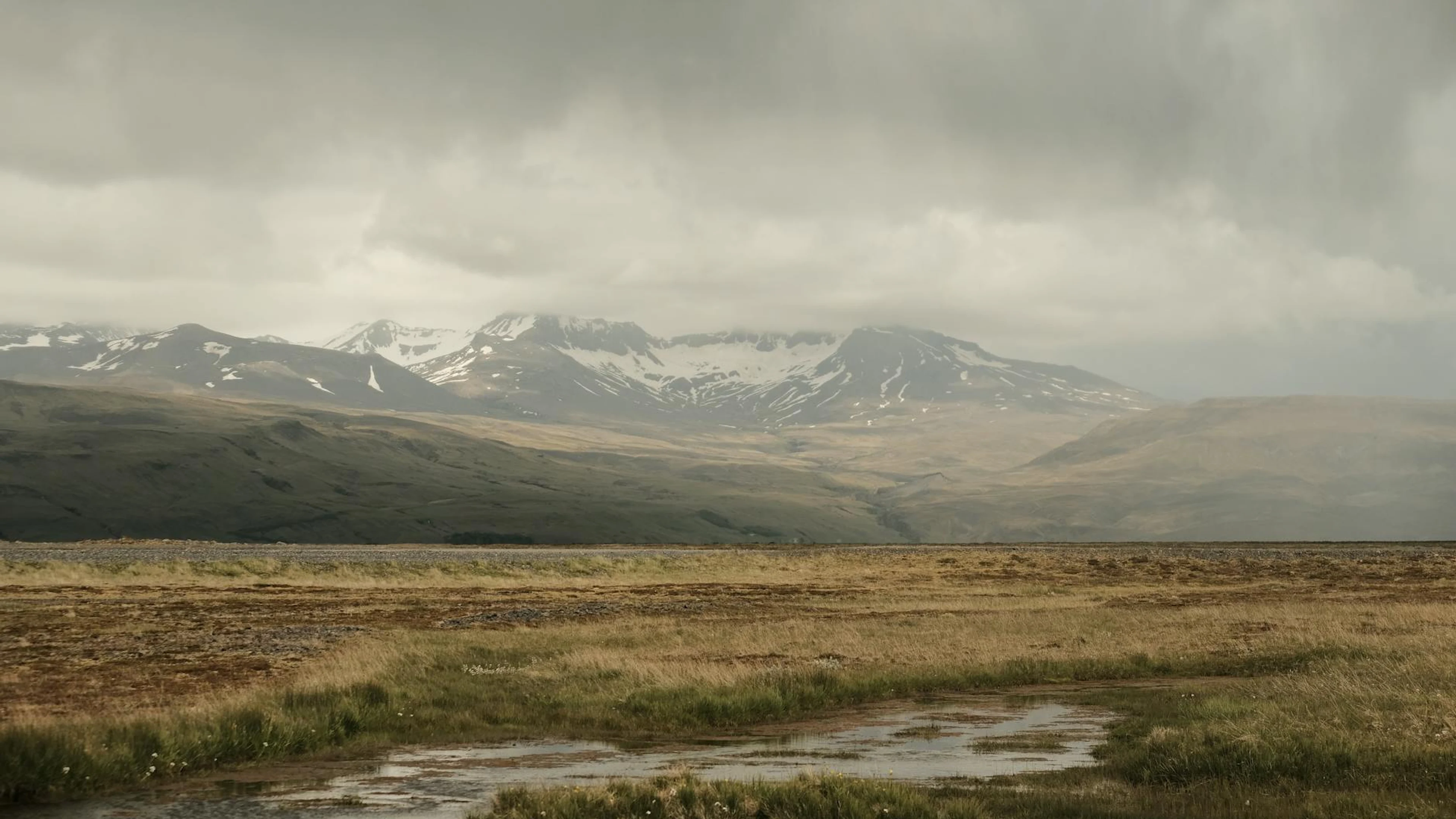 Wide view of the Icelandic tundra with snow-capped mountains and a cloudy sky. - free 4K Ultra HD mountain wallpaper for desktop