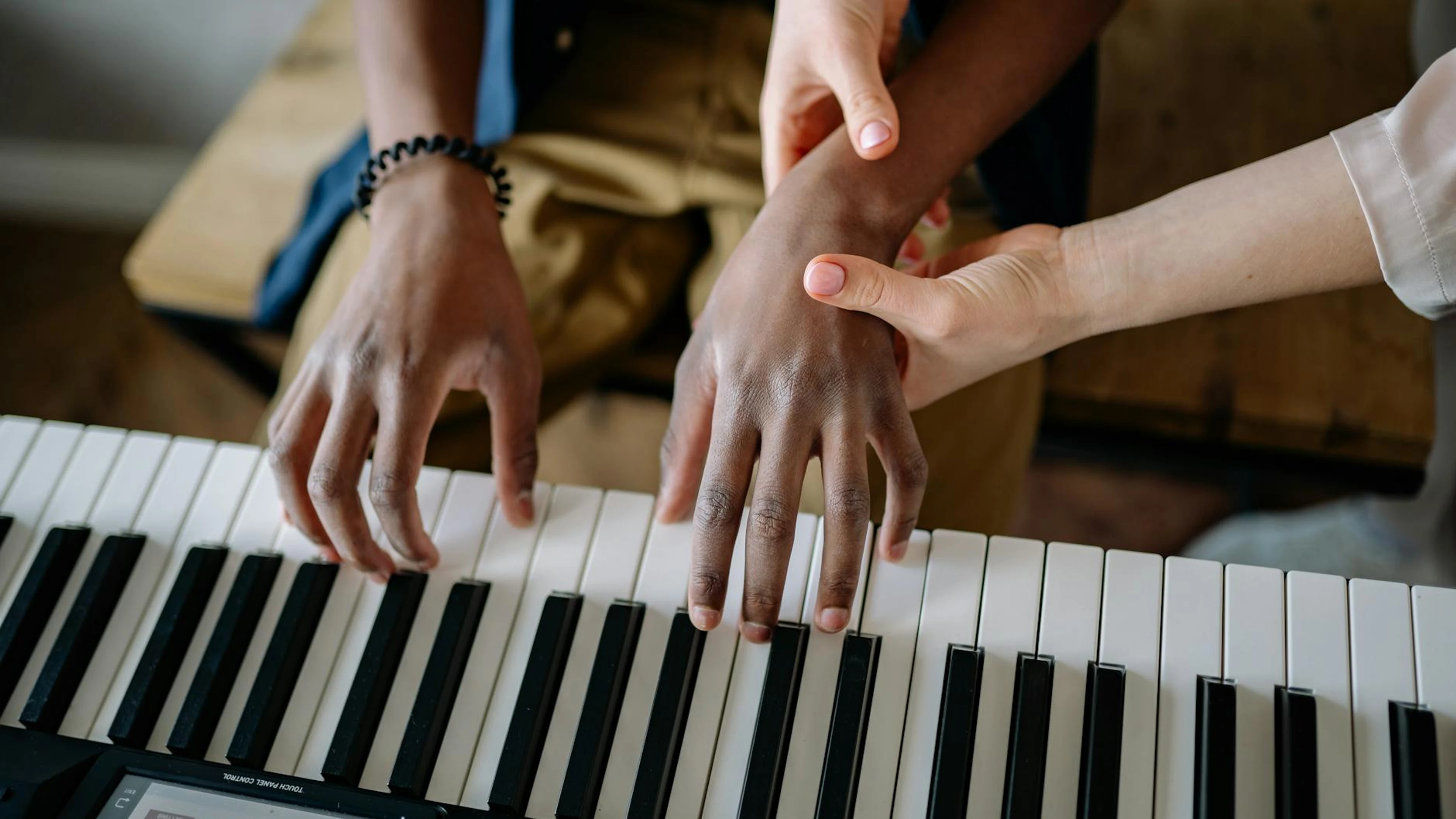 A music teacher guides a student on piano keys, emphasizing hands-on learning. - free 4K Ultra HD music wallpaper for desktop
