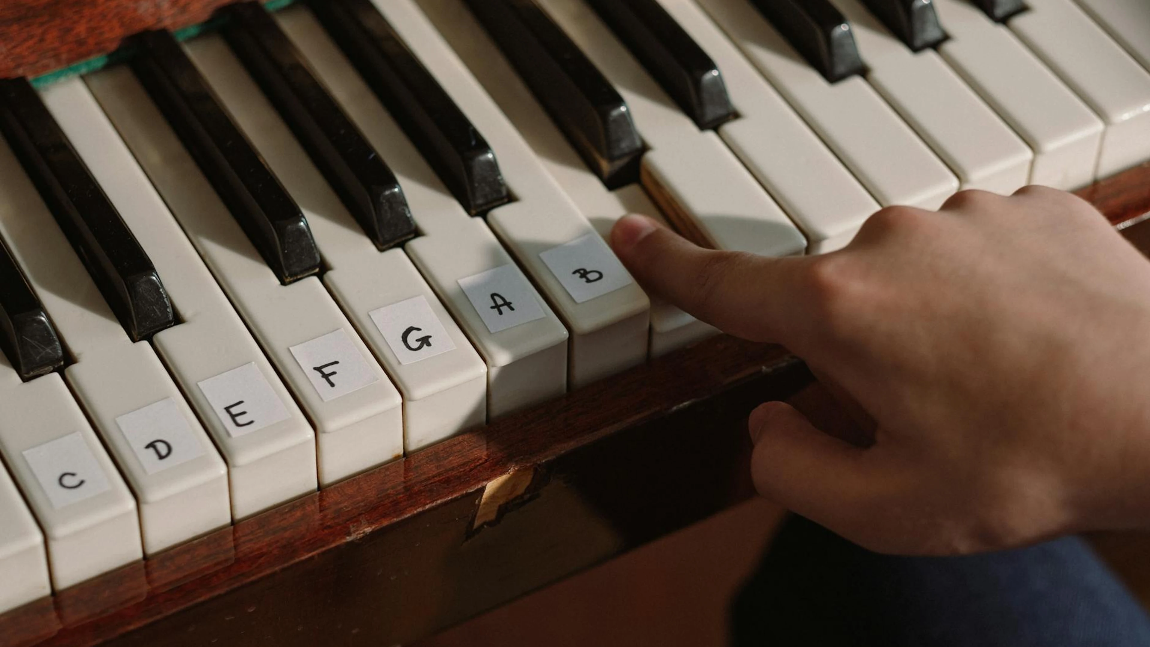 A person playing a labeled piano keyboard with finger pressing notes for learnin - free 4K Ultra HD music wallpaper for desktop