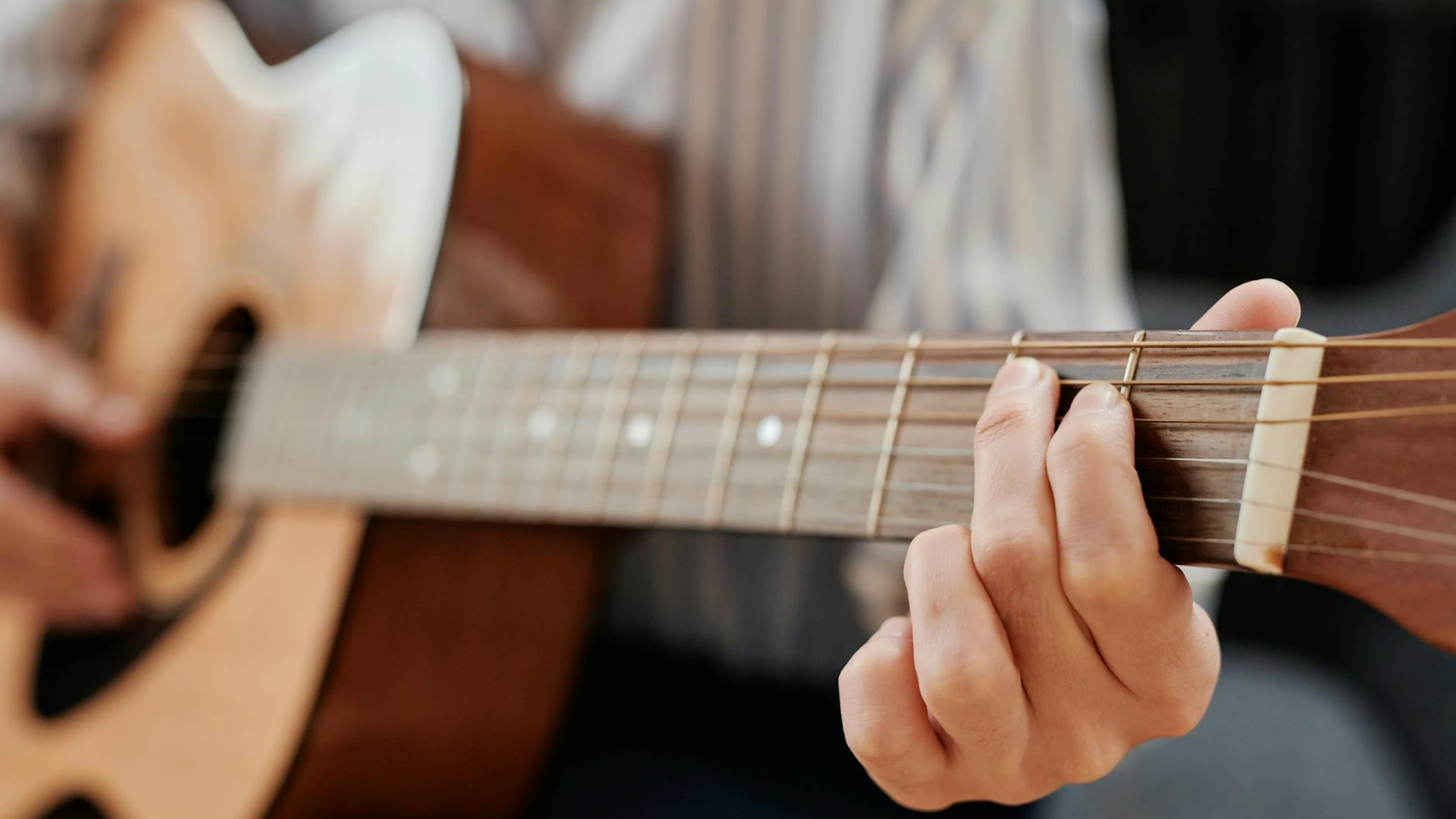 A person strumming chords on an acoustic guitar, focusing on fretboard technique - free 4K Ultra HD music wallpaper for desktop