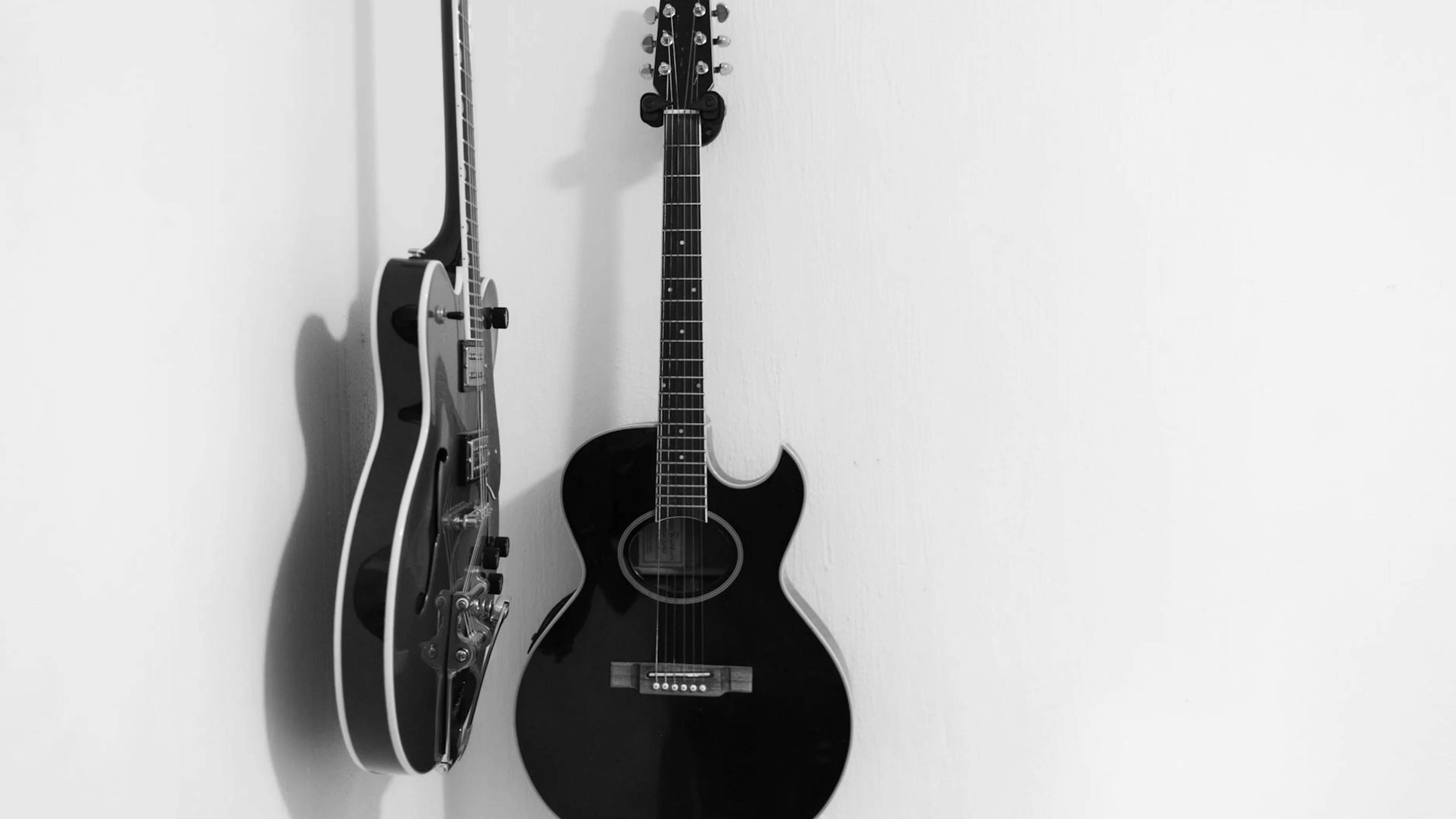 A sleek black acoustic guitar and an elegant electric guitar hang stylishly on a - free 4K Ultra HD music wallpaper for desktop