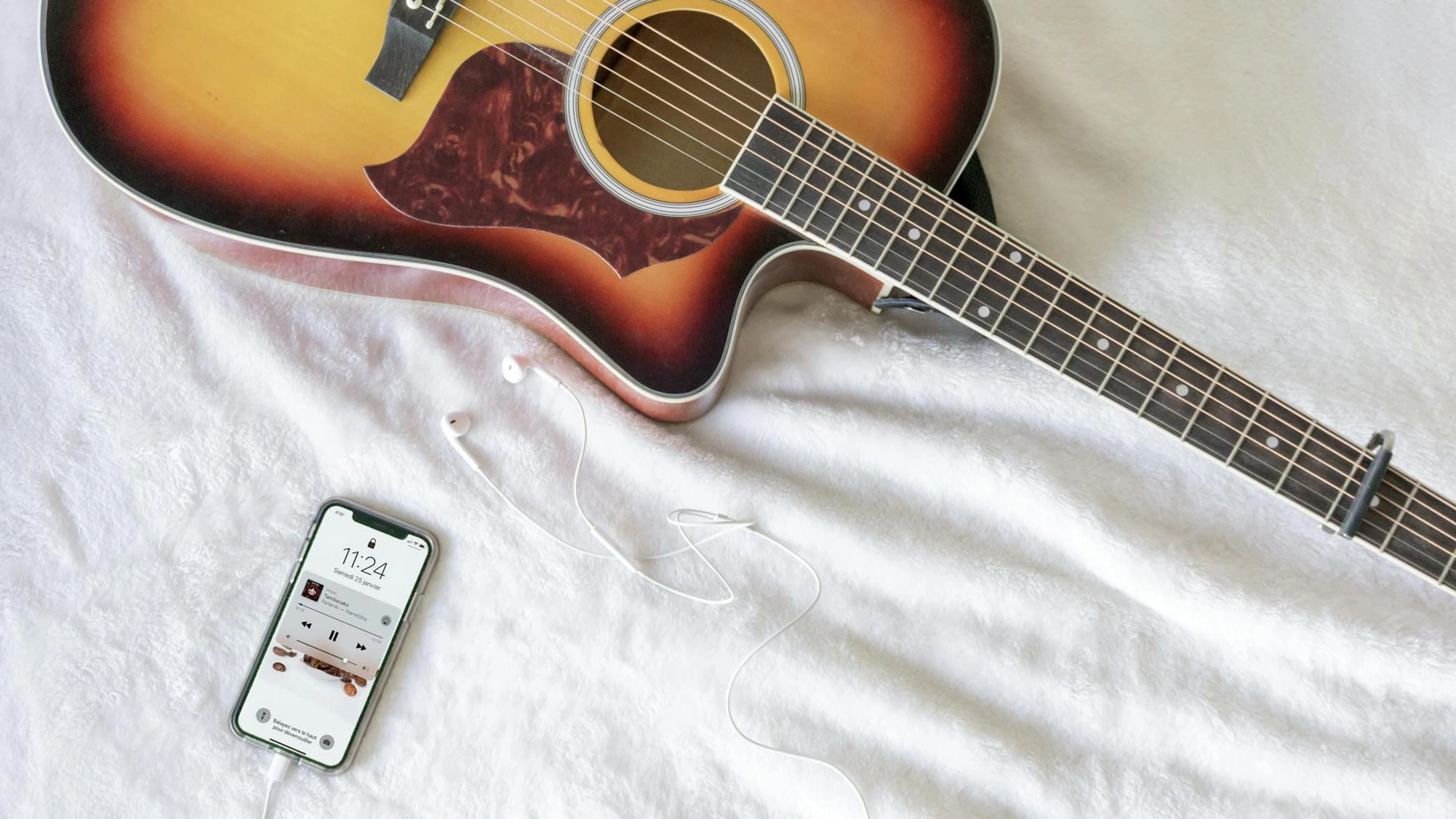 Acoustic guitar with smartphone playing music, headphones on soft white fabric. - free 4K Ultra HD music wallpaper for desktop