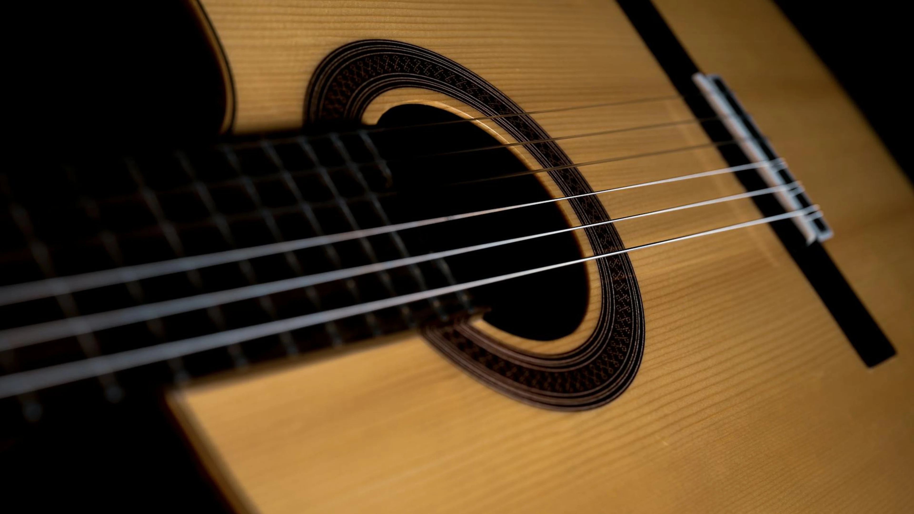 Detailed close-up of a classical acoustic guitar showing the strings and sound h - free 4K Ultra HD music wallpaper for desktop