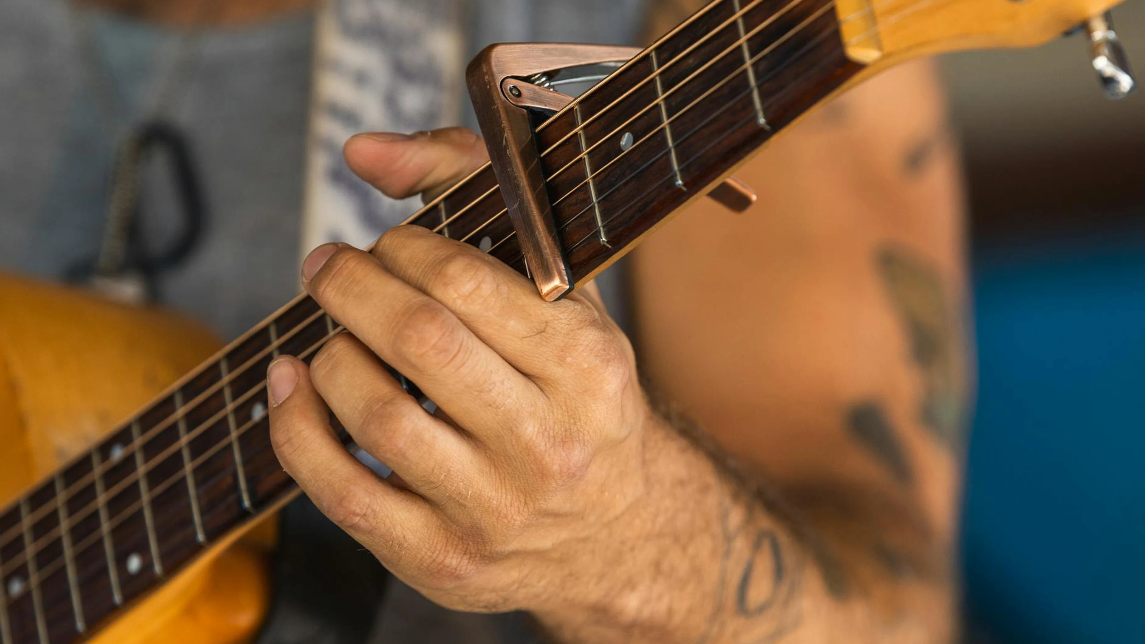 Detailed shot of a musician's hand playing an acoustic guitar using a capo. Perf - free 4K Ultra HD music wallpaper for desktop