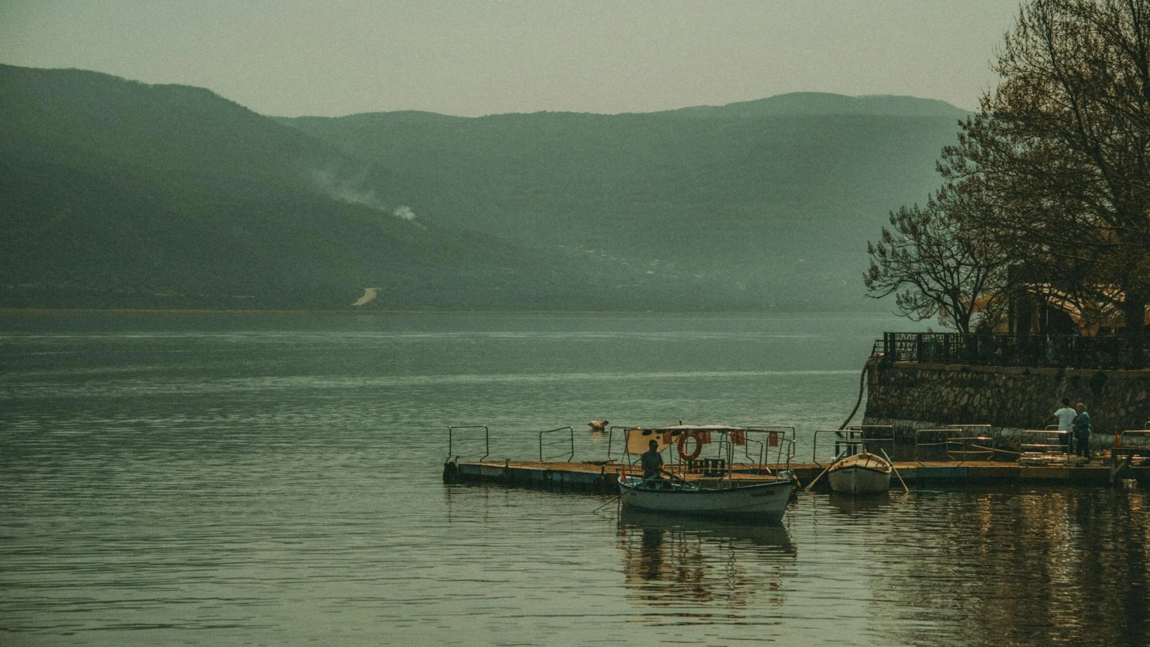 A peaceful lake view with a wooden pier, boats, and distant mountains under a mu - free 4K Ultra HD nature wallpaper for desktop