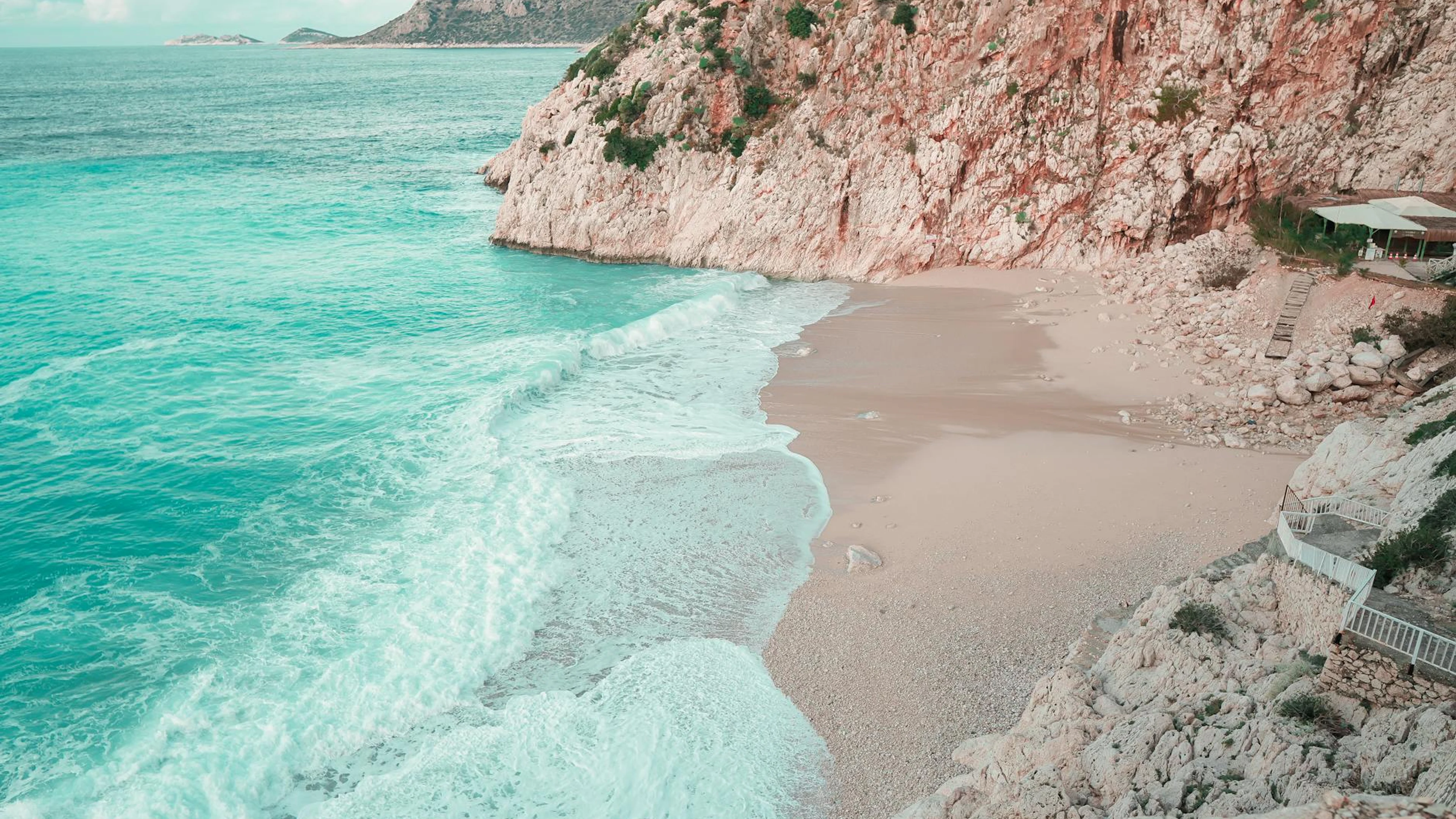 Serene view of sandy beach with waves crashing against rocky cliffs in Antalya, - free 4K Ultra HD nature wallpaper for desktop