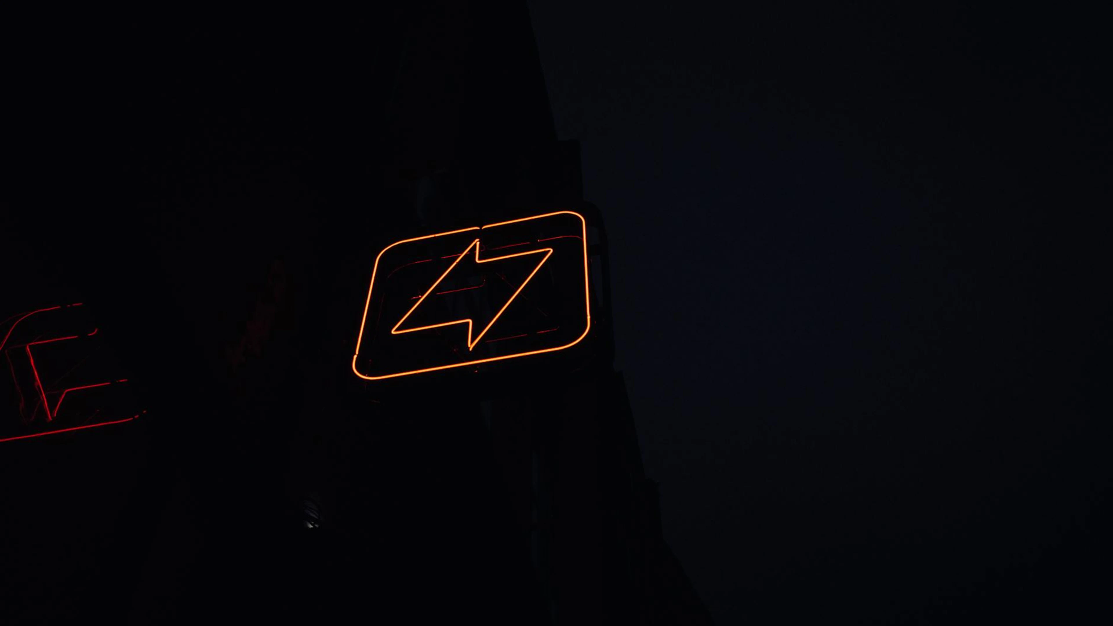 A glowing neon lightning bolt sign against a dark night background, symbolizing - free 4K Ultra HD neon wallpaper for desktop