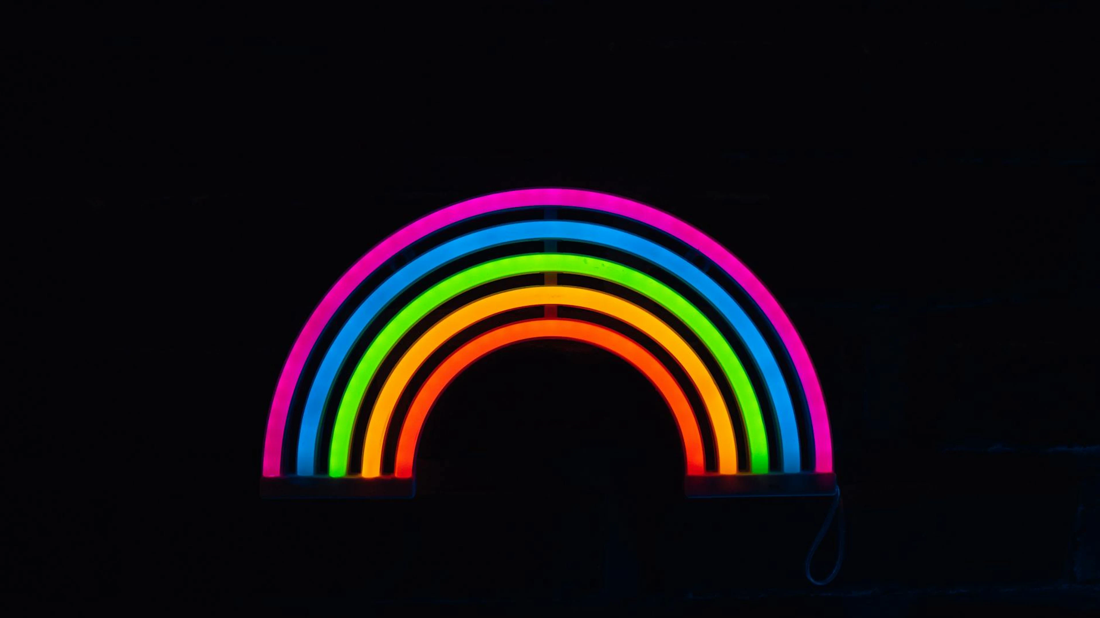 A glowing neon rainbow against a dark background, showcasing colorful LED lights - free 4K Ultra HD neon wallpaper for desktop