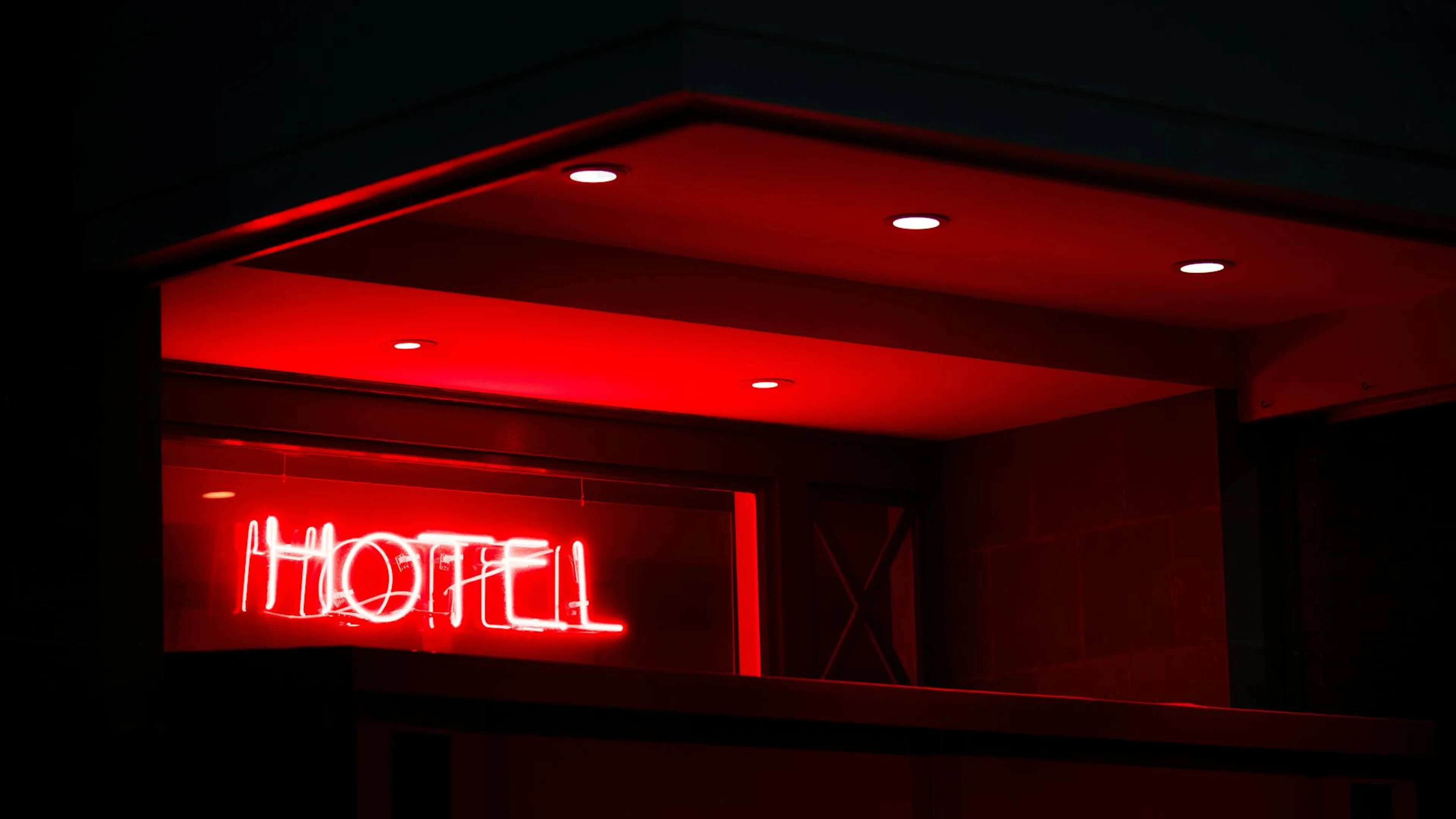 A vibrant red neon sign reading 'Hotel' glows in the night, casting a modern amb - free 4K Ultra HD neon wallpaper for desktop