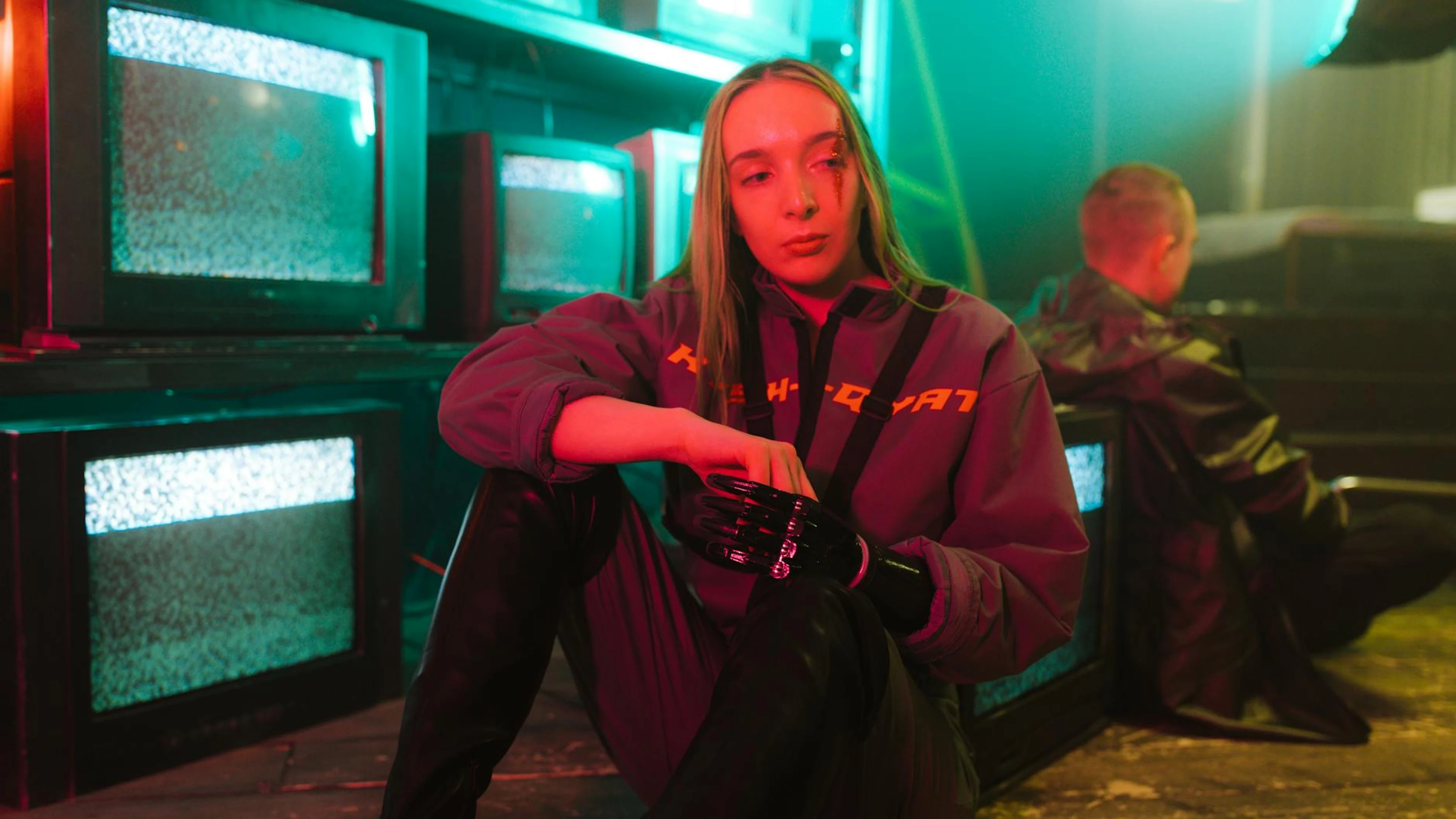 A woman with a prosthetic hand sits near old TVs in a cyberpunk-themed room. - free 4K Ultra HD neon wallpaper for desktop