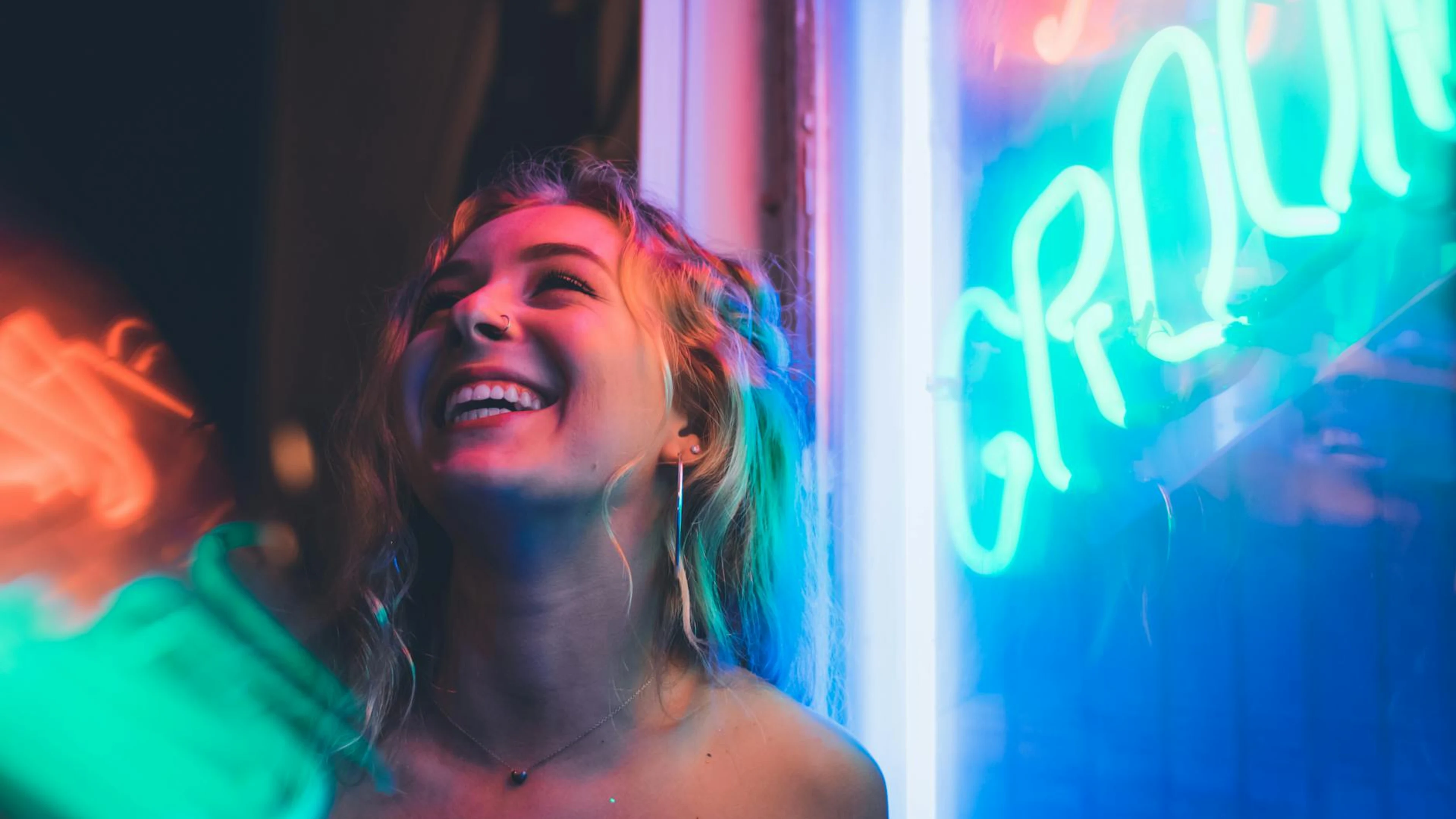 Smiling woman enjoying nightlife with vibrant neon signs, capturing a lively moo - free 4K Ultra HD neon wallpaper for desktop