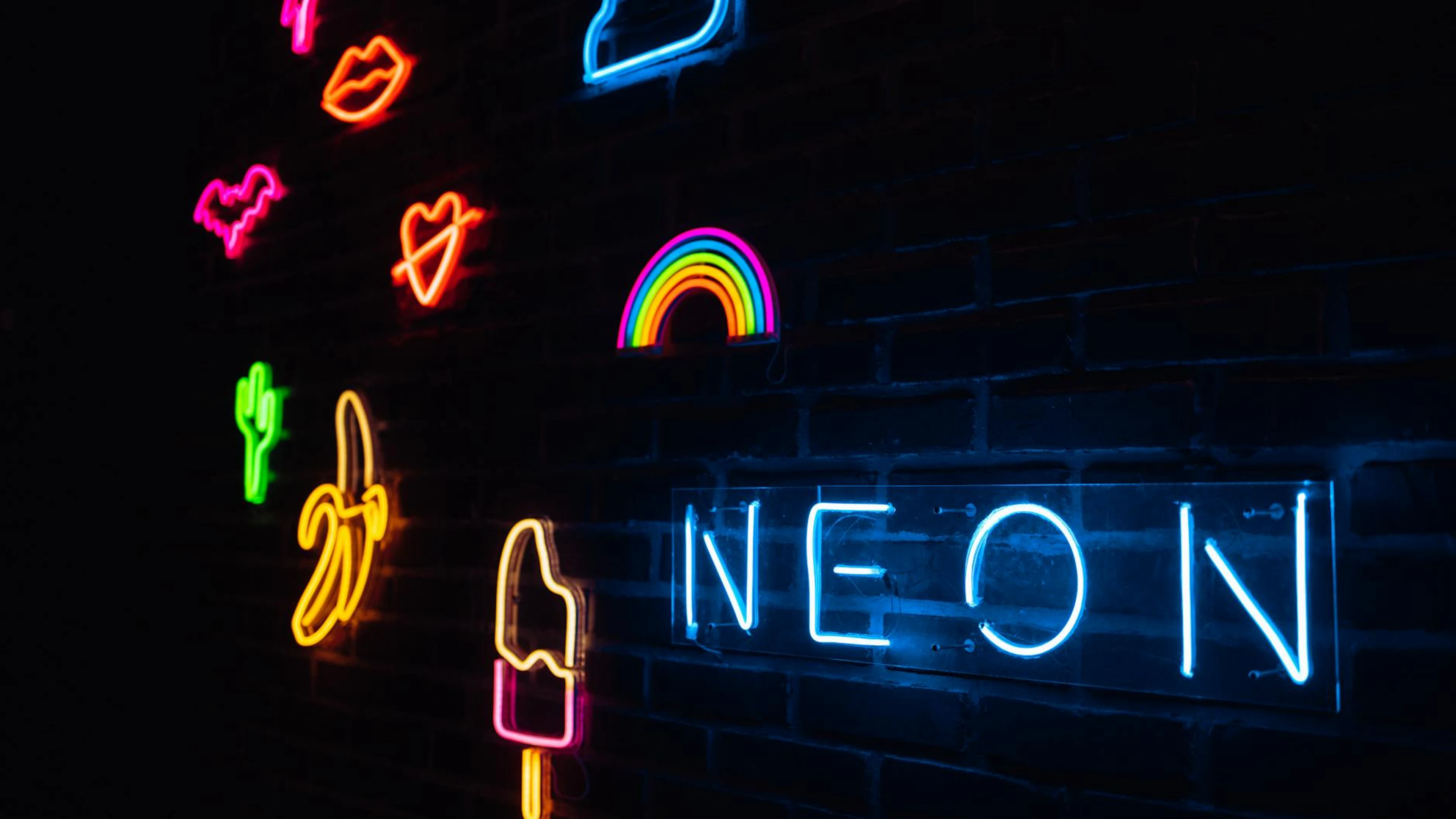 Vibrant neon signs illuminated on a dark brick wall with various shapes and colo - free 4K Ultra HD neon wallpaper for desktop